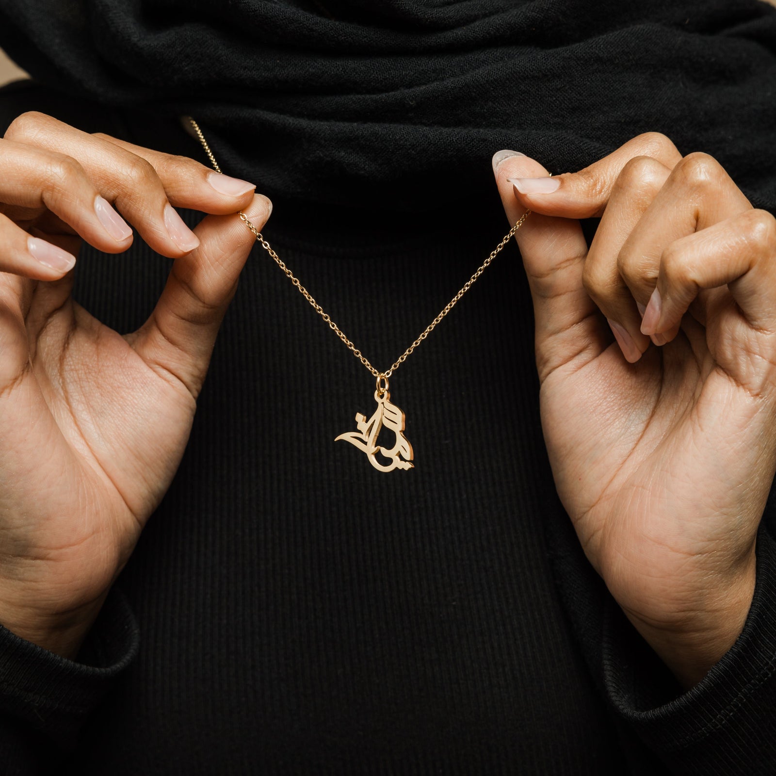 Close up of the gold Ready Calligraphy Name Necklace as the model pulls the chain to show its design.