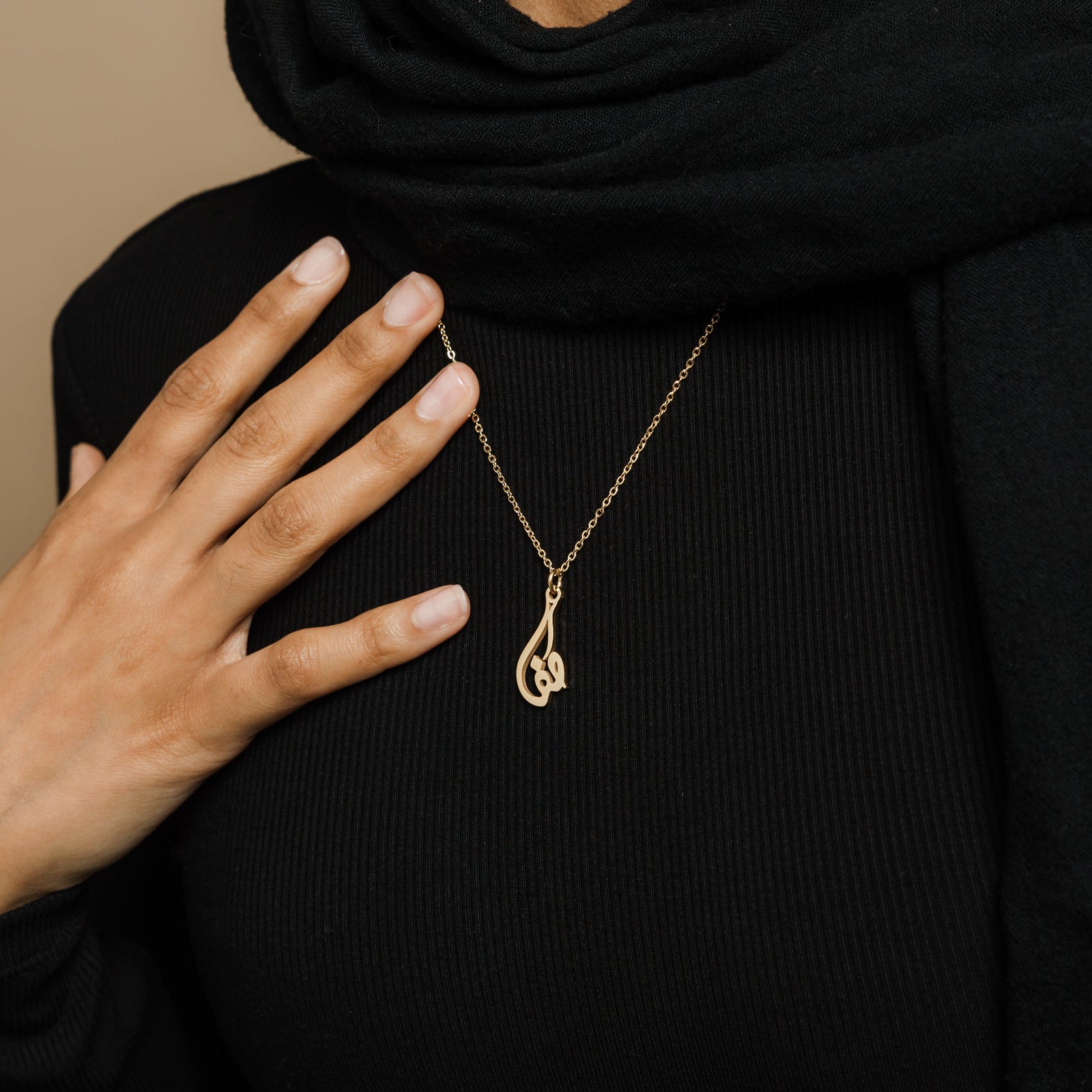 the gold Ready Calligraphy Name Necklace against the black fabric of the model's clothing