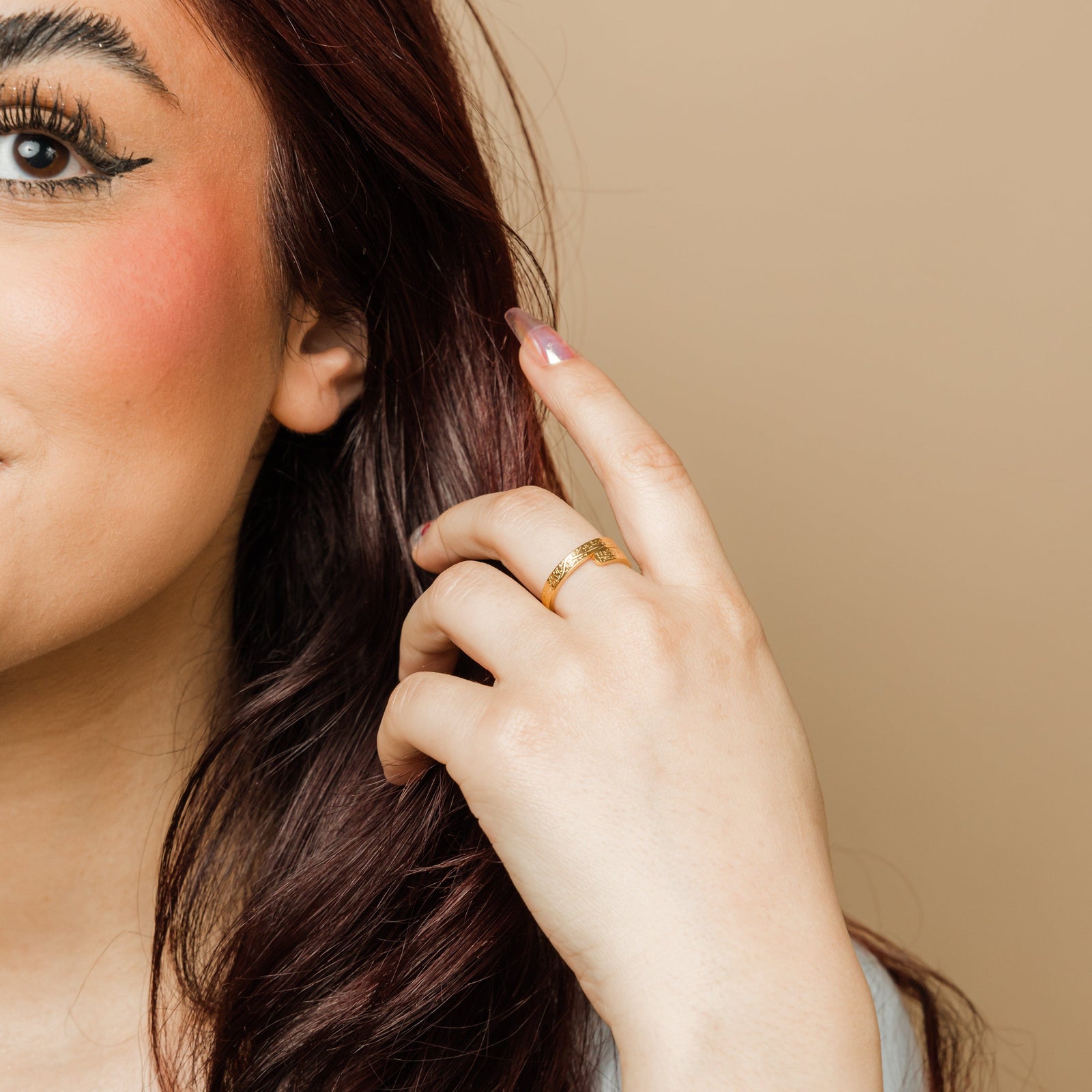 Woman wearing a gold thikr wrap ring with Arabic calligraphy, her hand raised near her face