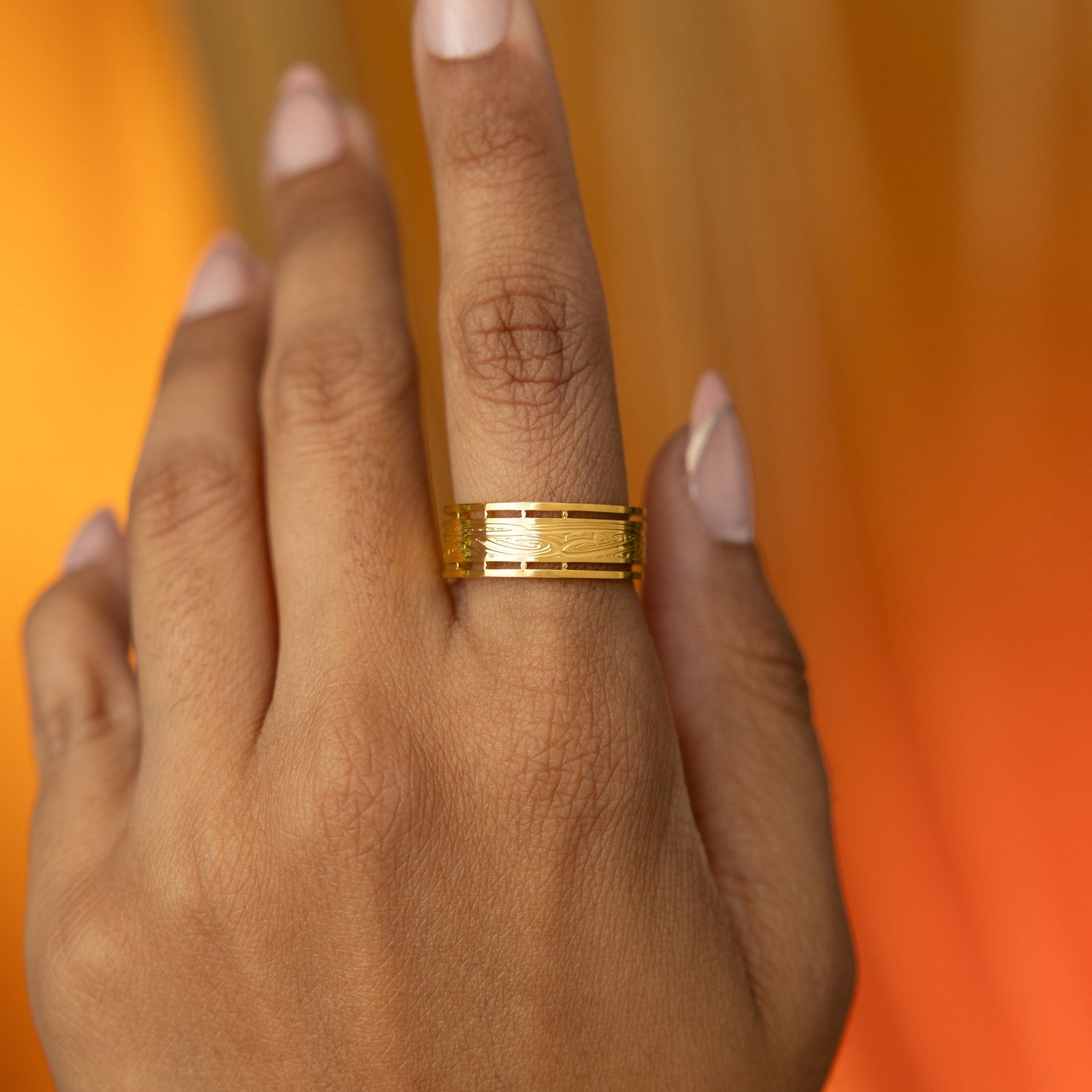 Hand showcasing the Sabireen ring in gold, the wide band engraved with Arabic calligraphy and bordered with geometric cutouts.