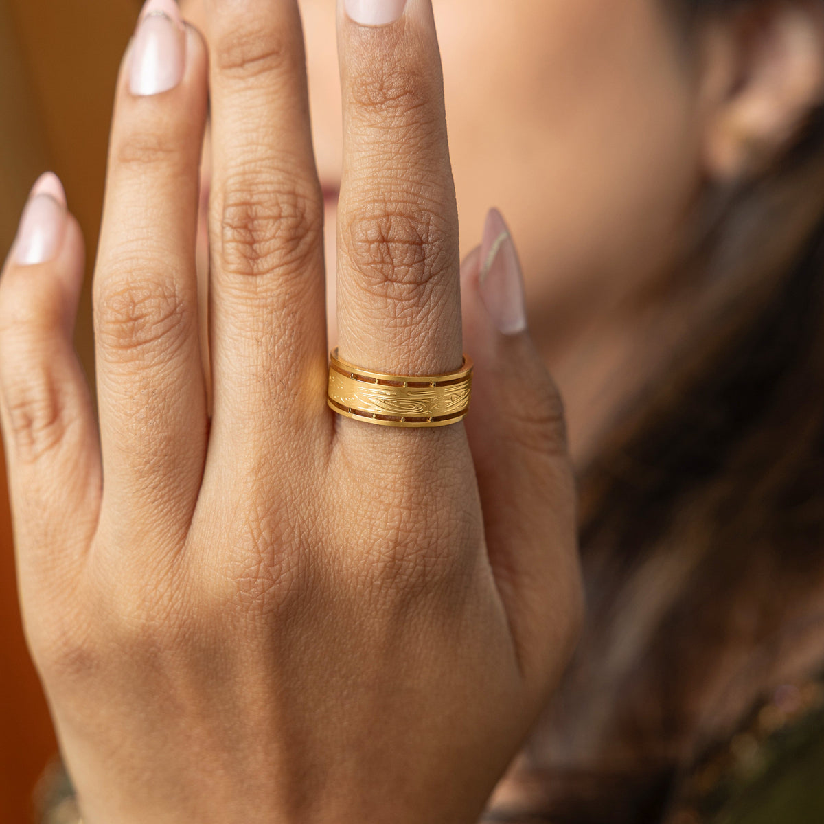 Hand wearing the gold Sabireen ring with carved Arabic calligraphy details.