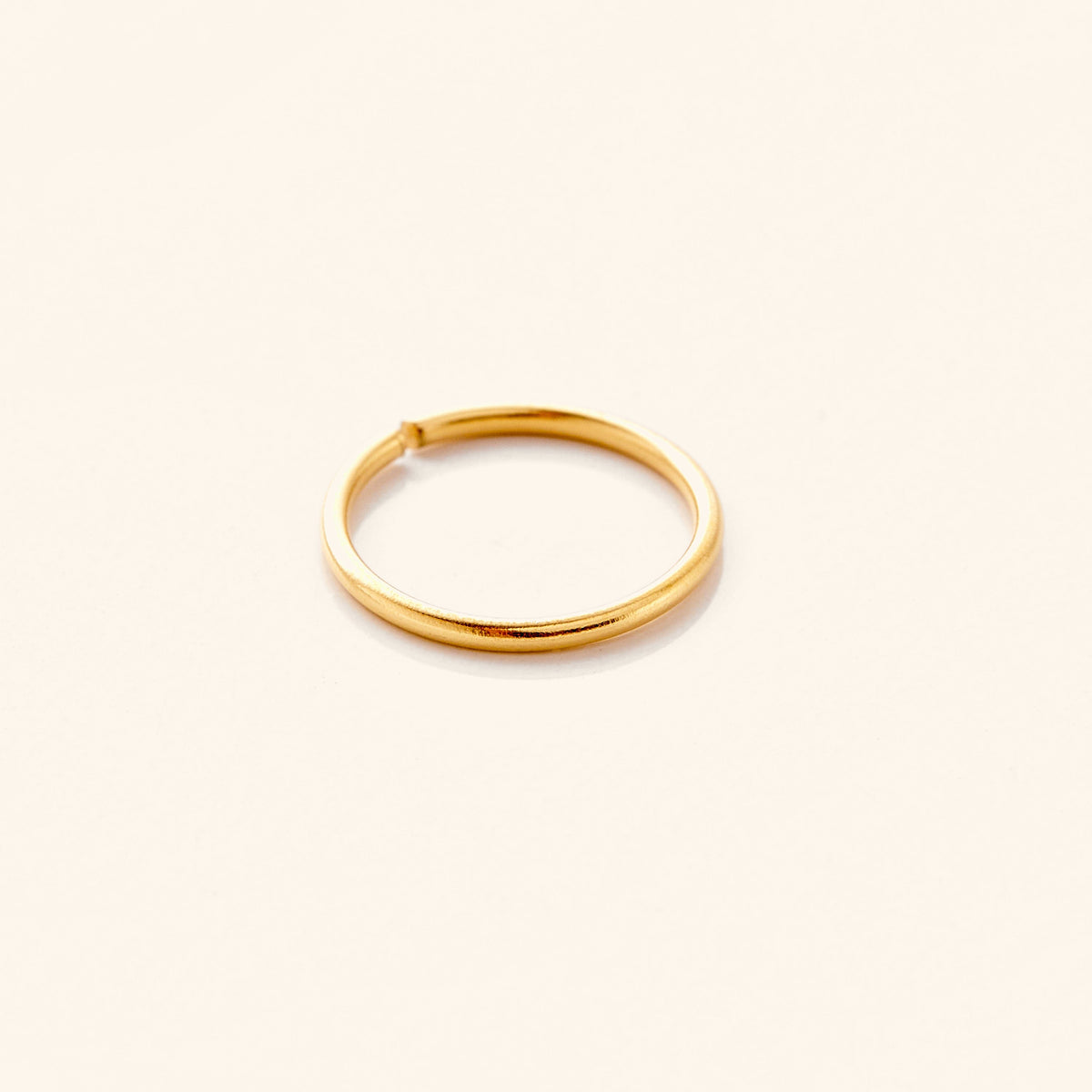 Photo of an 18k gold plated minimalistic nose hoop against a light background.