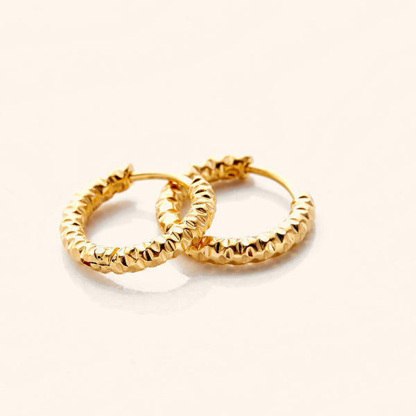 Photo of a pair of 18k gold plated hoop earrings. The Flake Hoops have the silhouette of classic hoops, with an added flair in its imperfect edges that give it a glowing vintage.