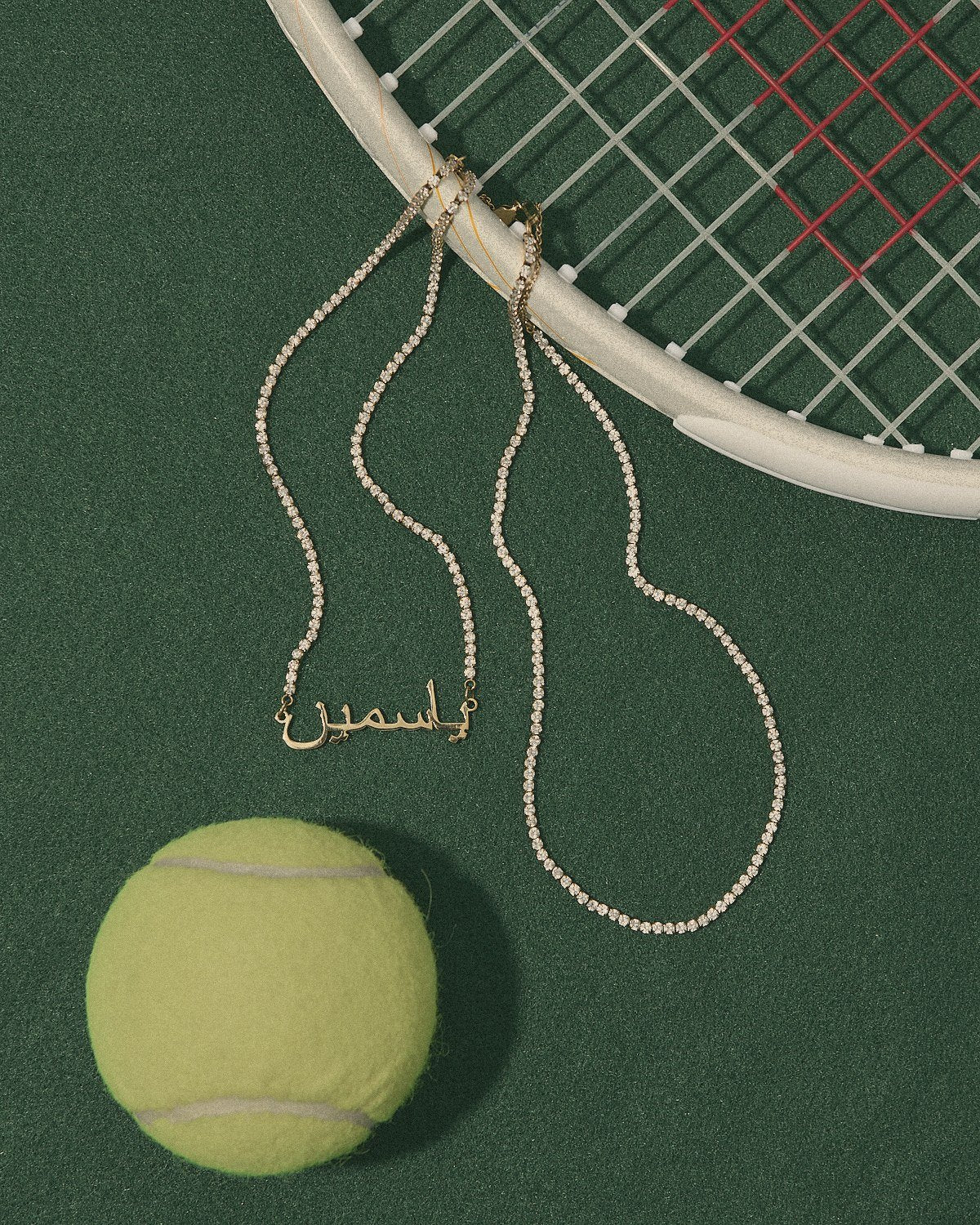 Gold custom tennis name necklace on green court turf with a tennis racket and ball