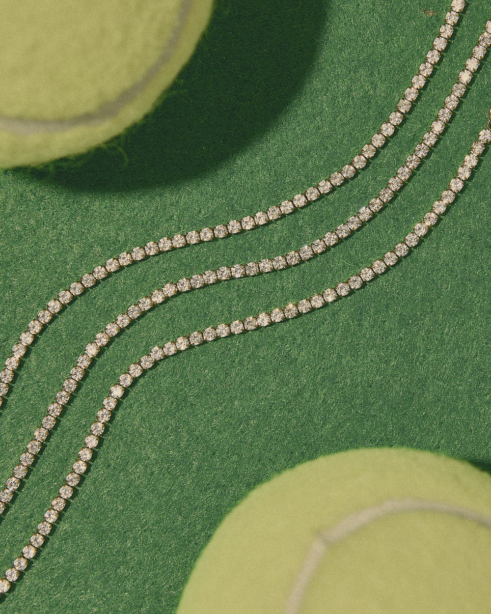 Three gold tennis chains laid across green court turf beside tennis balls