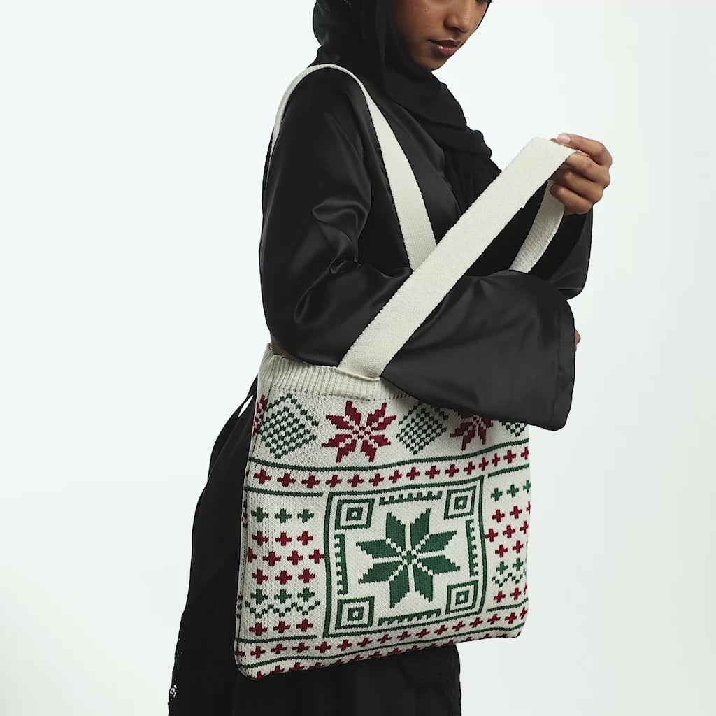 Model carrying the Knit Crochet Tatreez Tote on their right shoulder. close up of the design of the tote bag. Model holds the bag by its strap then opens the inner compartment.