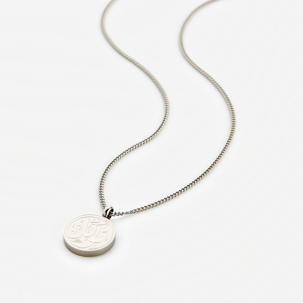 Silver necklace with a circular pendant engraved with 'Tawakkul' calligraphy, displayed on a white background.