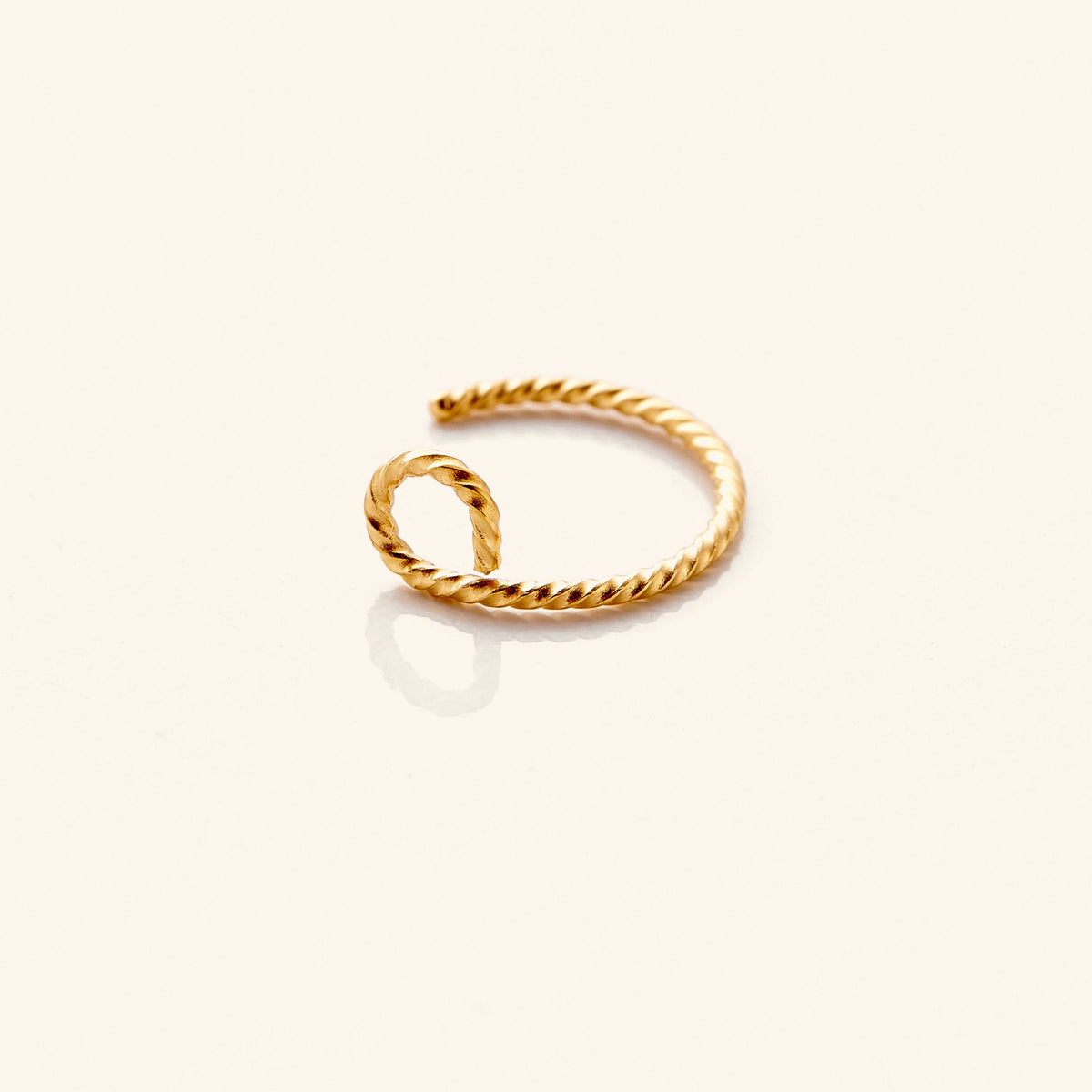 Photo of an 18k gold plated nose hoop marked with a spiraling patter against a light background.