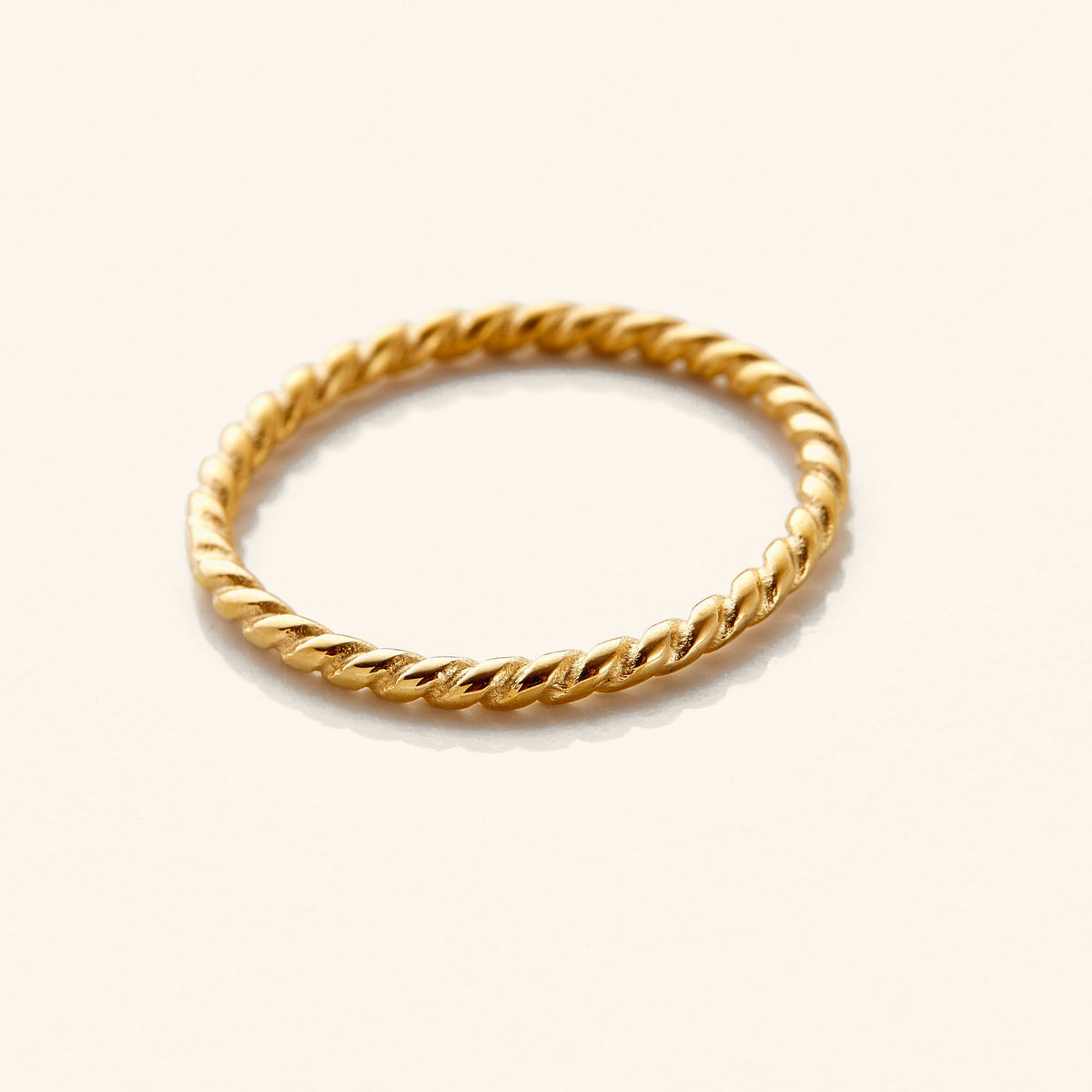 Gold twist ring featuring a delicate rope-like design with a polished finish, displayed flat on a white surface.