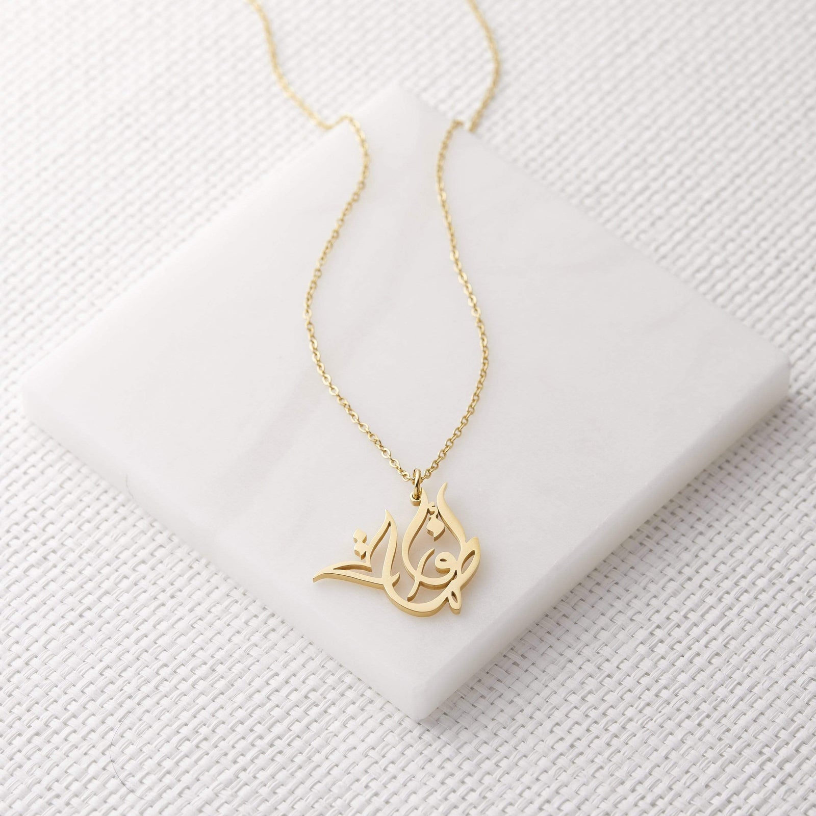Close up of the gold Ready Calligraphy Name Necklace against a light background.