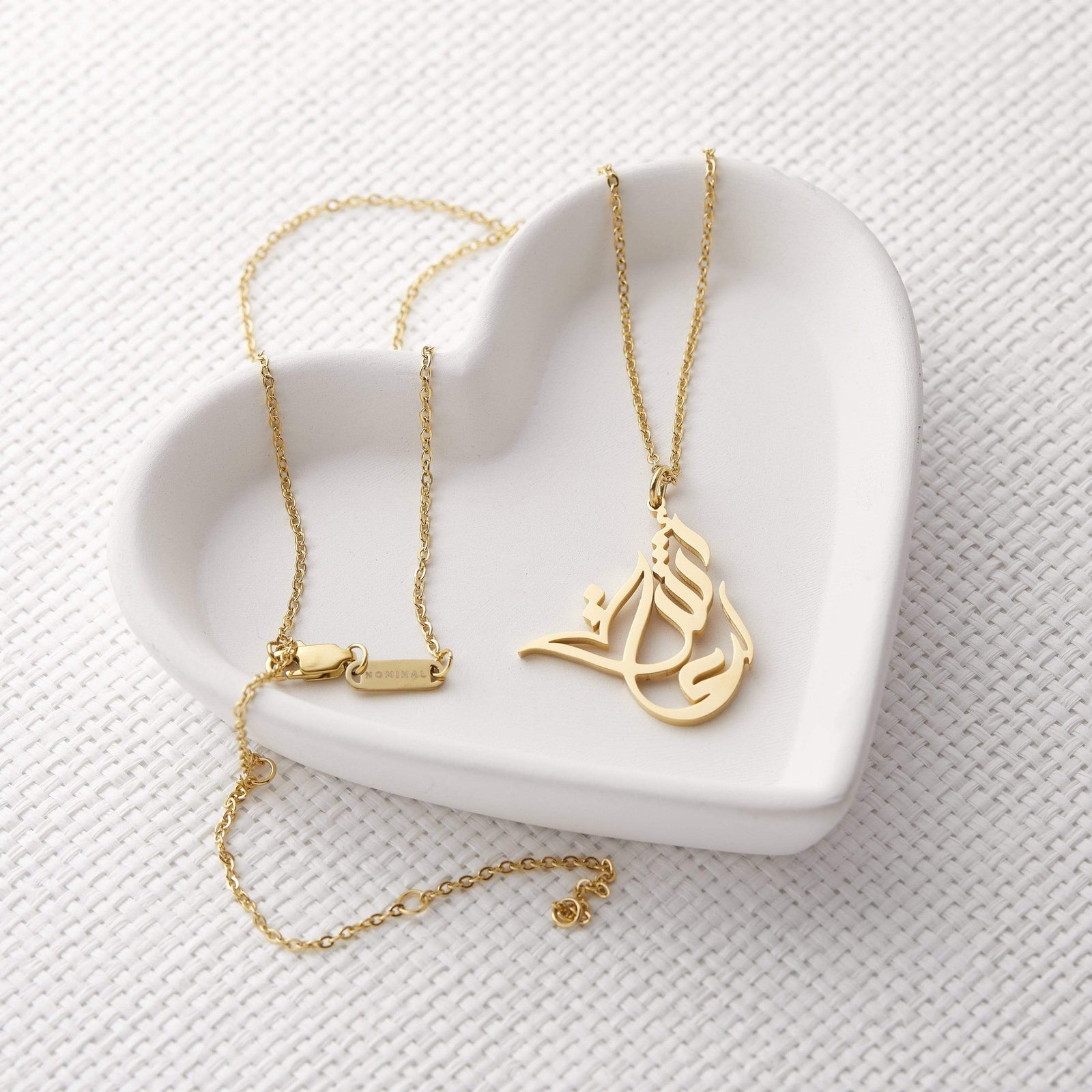Photo of a gold Ready Calligraphy Name Necklace laid flat on a heart shaped plate.
