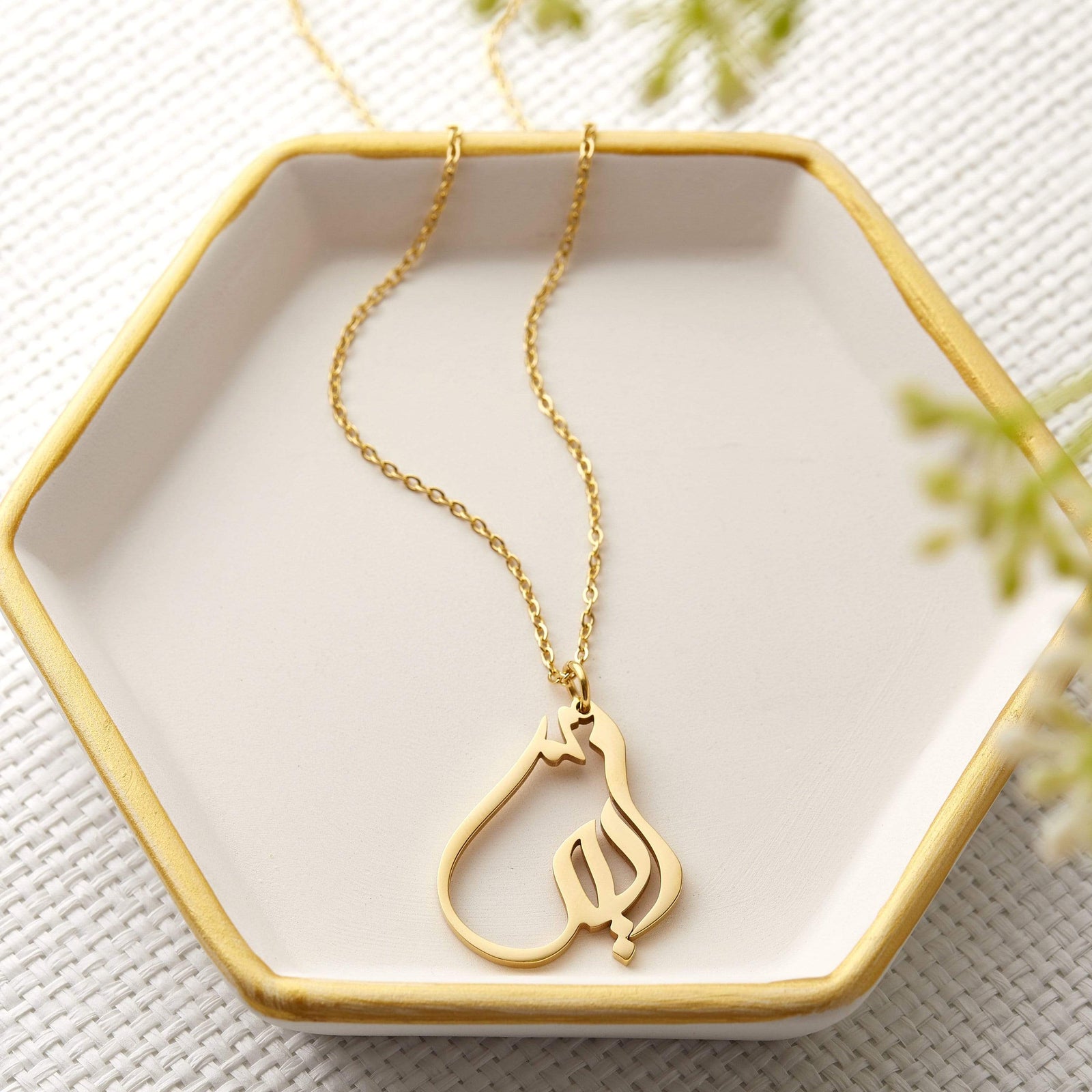 Photo of a gold Ready Calligraphy Name Necklace laid flat on a hexagon shaped plate.