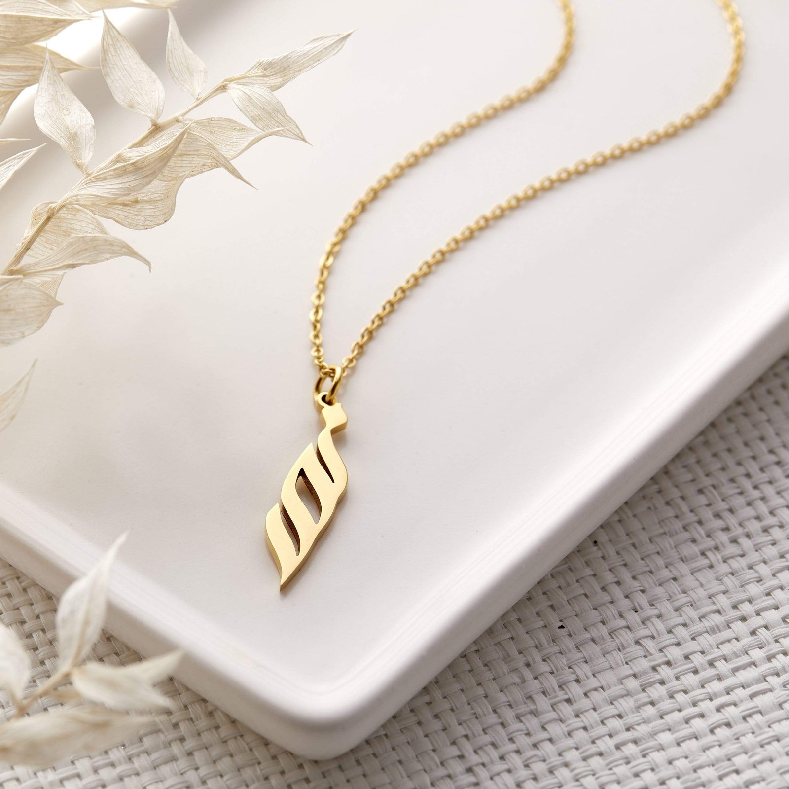 Photo of a gold Ready Calligraphy Name Necklace laid flat on a light colored plate.