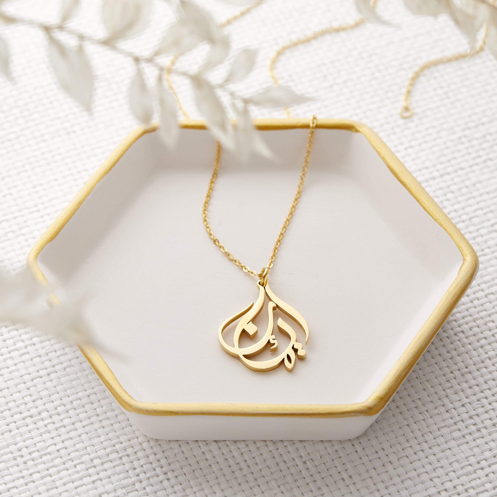 Photo of a gold Ready Calligraphy Name Necklace laid flat on a hexagon plate.