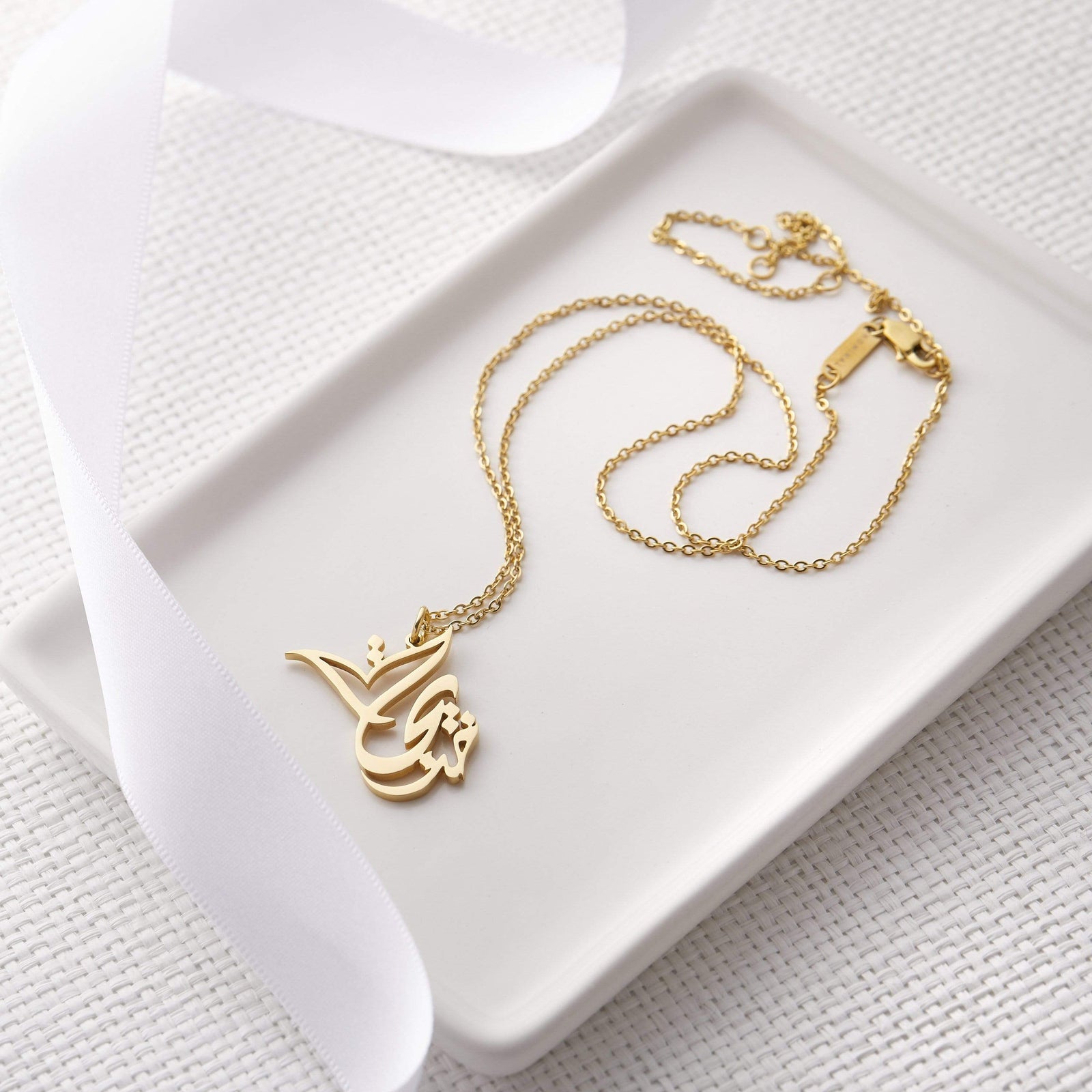 Photo of a gold Ready Calligraphy Name Necklace laid flat on a rectangular plate.