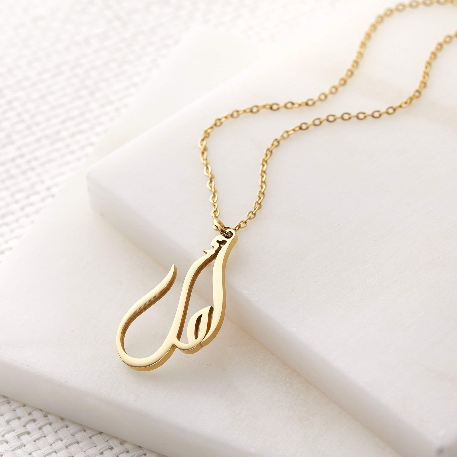 Close up of the gold Ready Calligraphy Name Necklace against a light background.