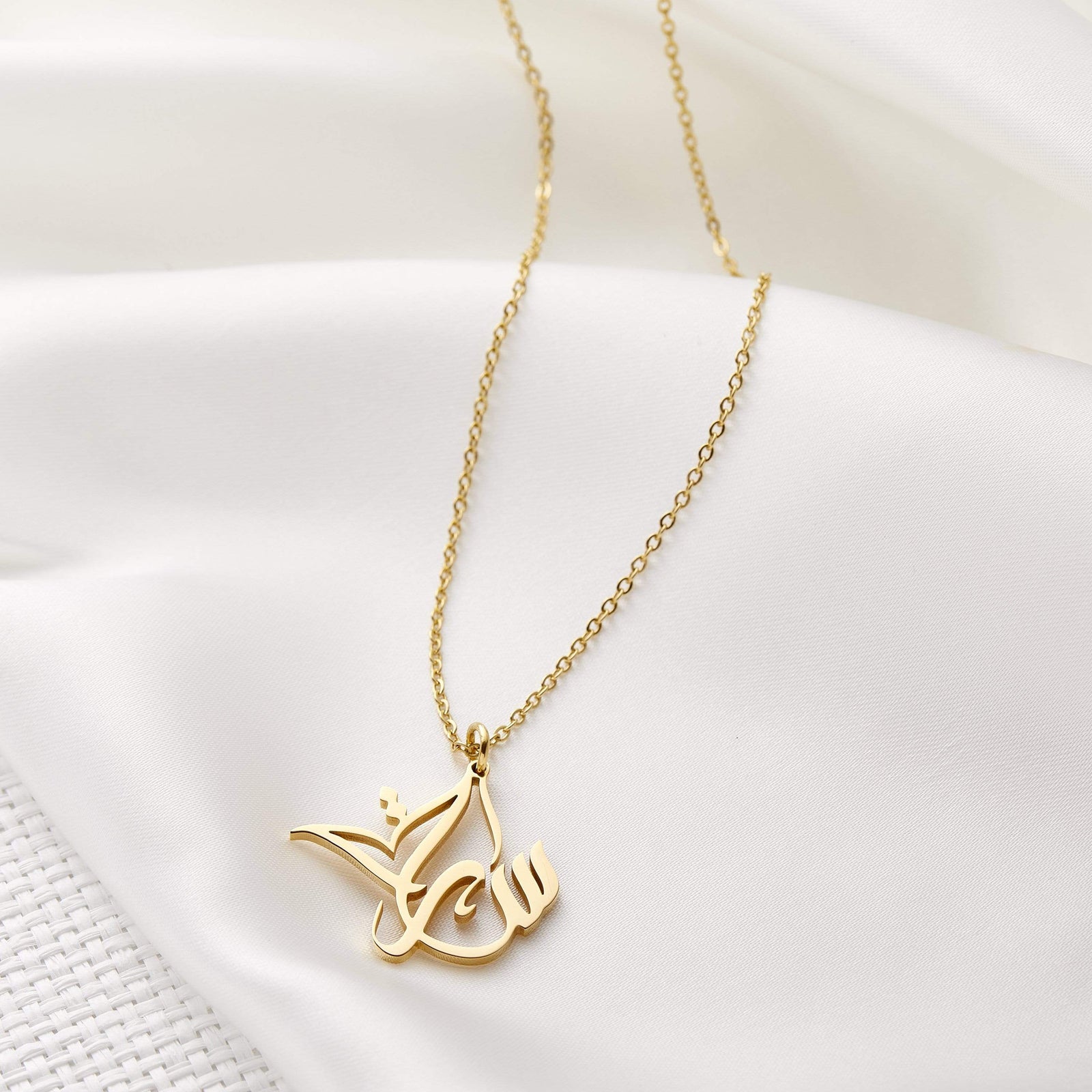 Close up of the gold Ready Calligraphy Name Necklace against a light background.