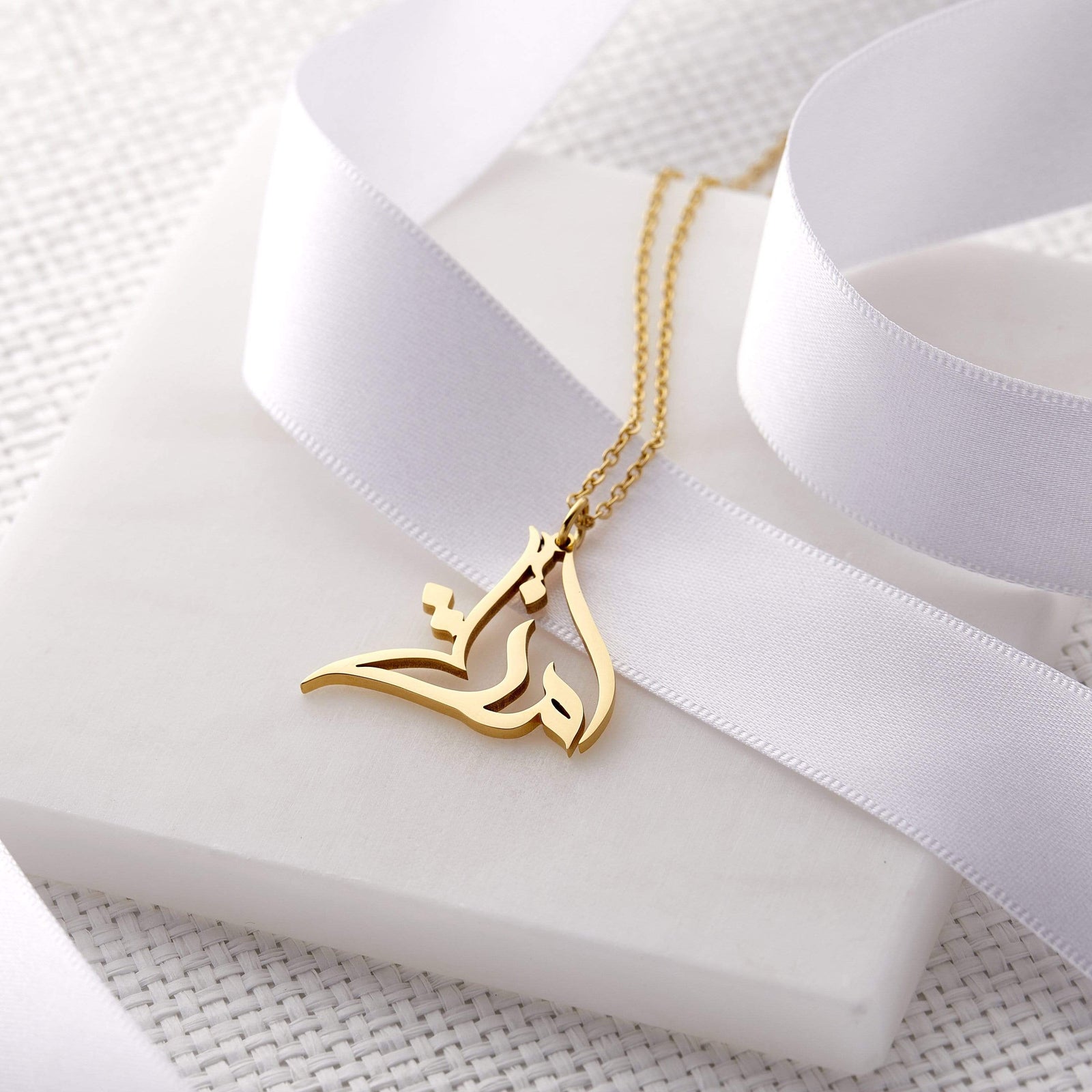 Close up of the gold Ready Calligraphy Name Necklace against a light background.