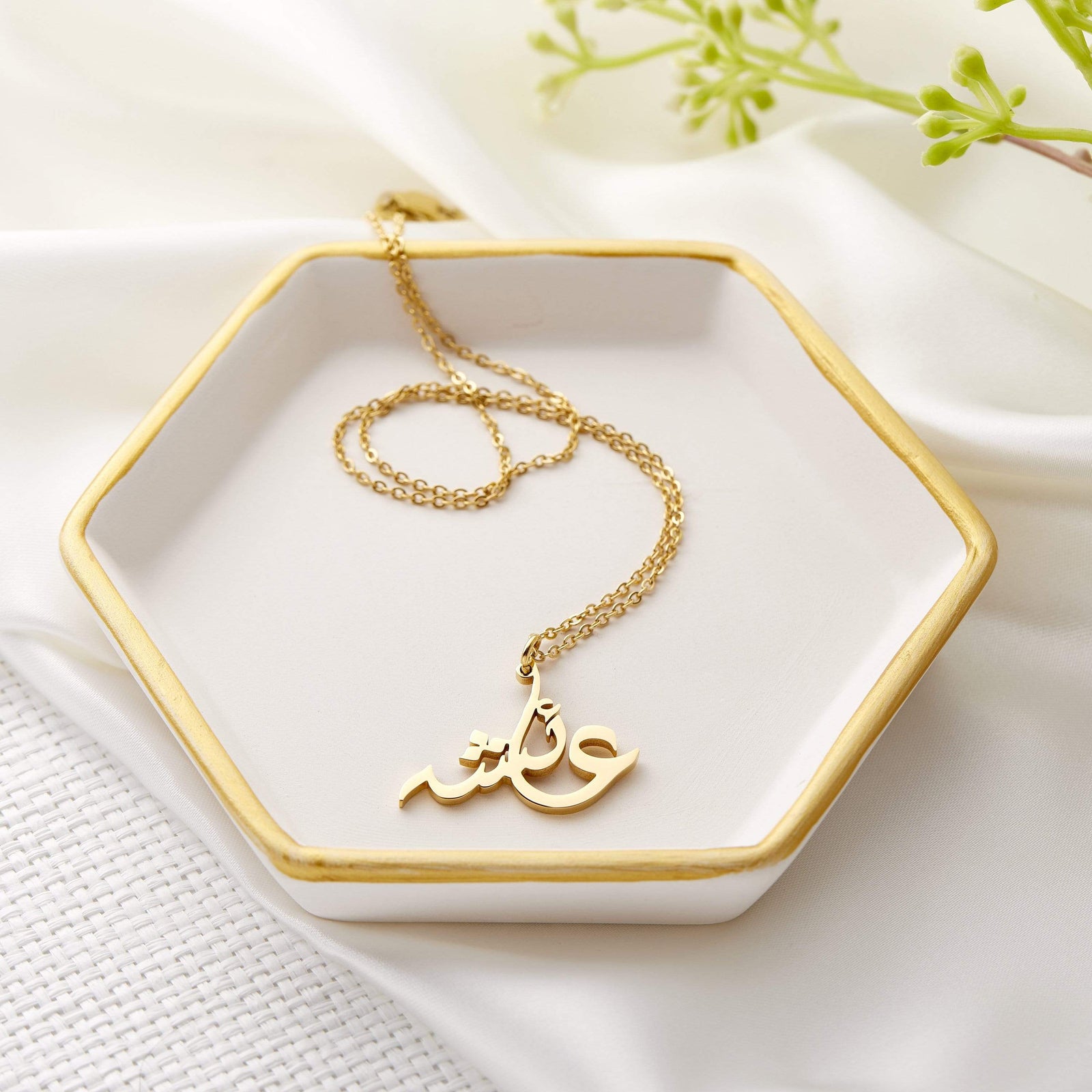 Close up of the gold Ready Calligraphy Name Necklace against a hexagon shaped plate