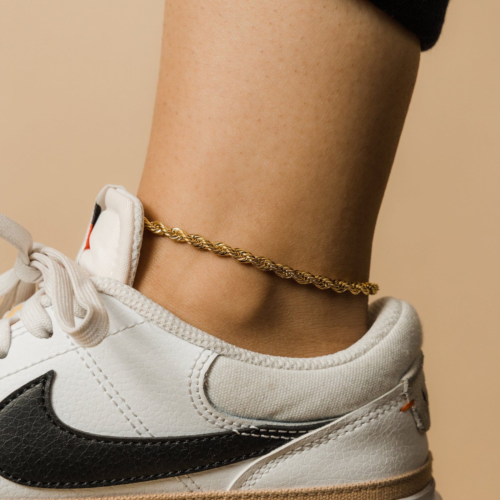 Close-up of a gold rope chain anklet on ankle paired with a white sneaker.