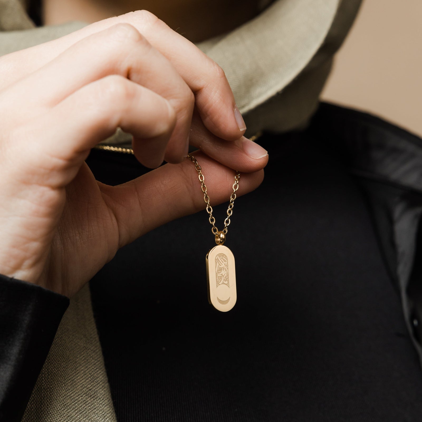 Close up of the gold Alhamdulillah Moon Necklace as the model lifts the chain to show the design of the pendant.