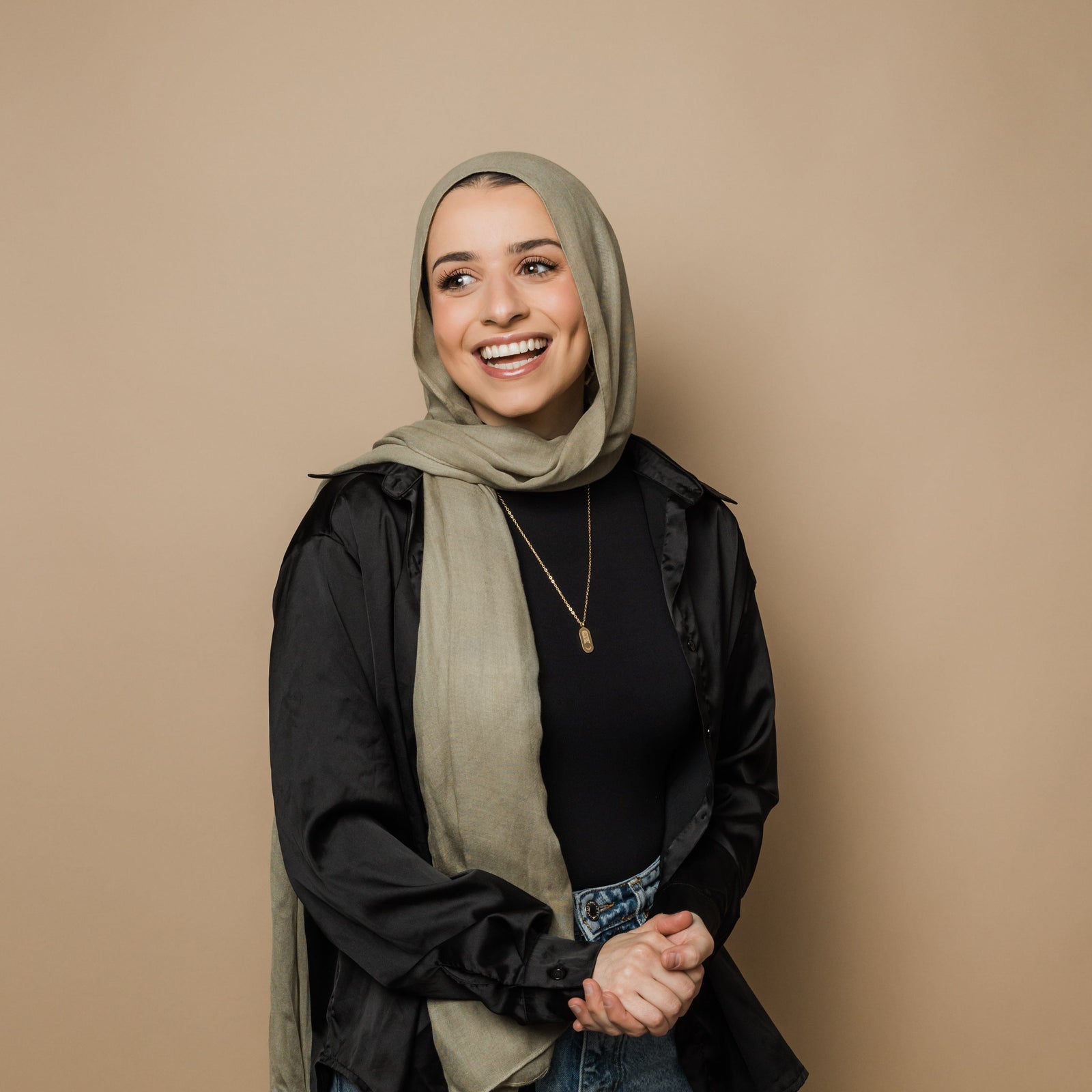 Photo do the model smiling with their hands clasped in front of them. The model is wearing the gold Alhamdulillah Moon Necklace.