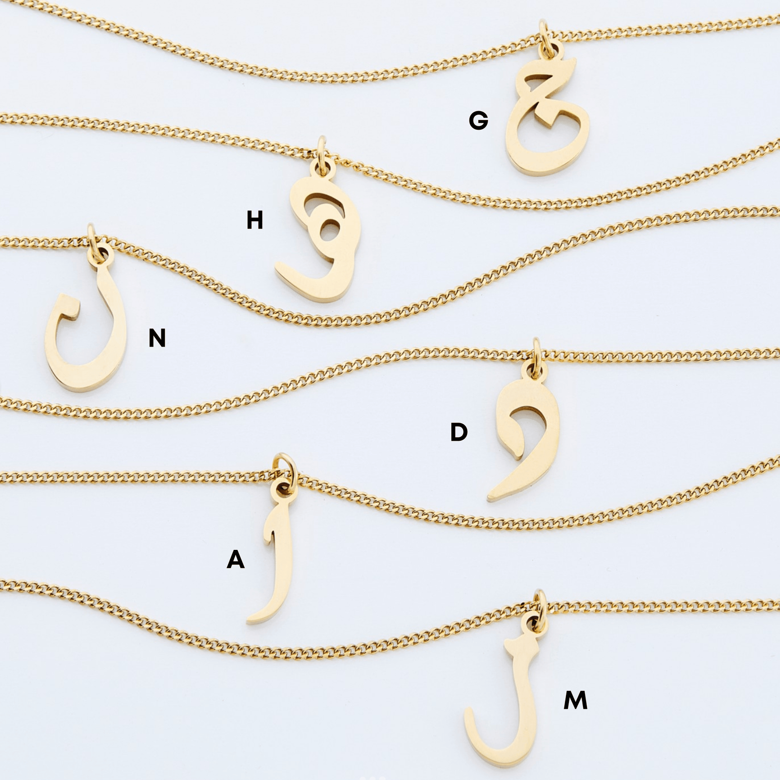Flat lay of six gold Hanging Arabic Letter Necklaces featuring G, H, N, D, A, and M.