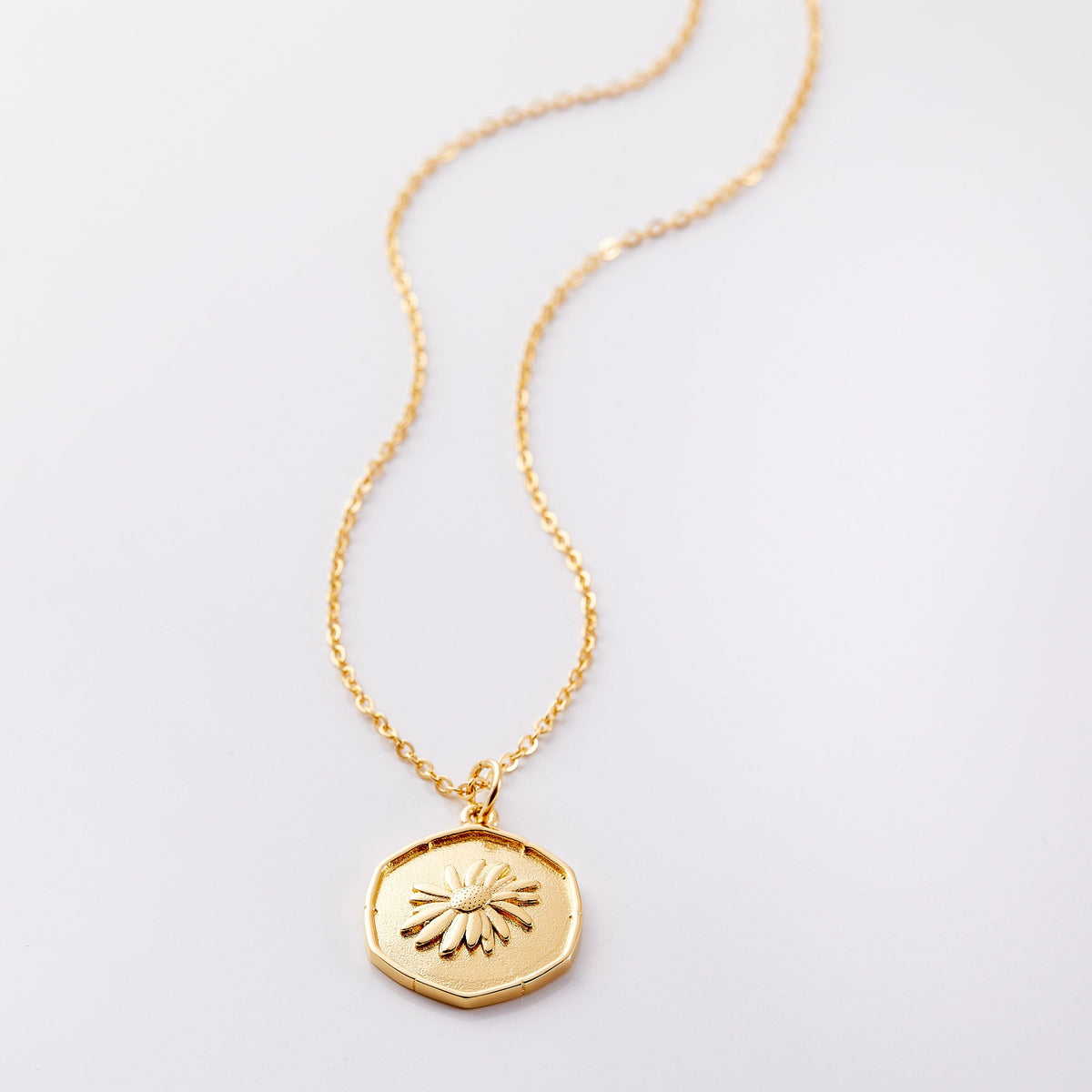 Photo of an 18k golf plated necklace with a pendant that is molded with an imperfect finish, the April Birth Flower is a daisy to represent love and purity