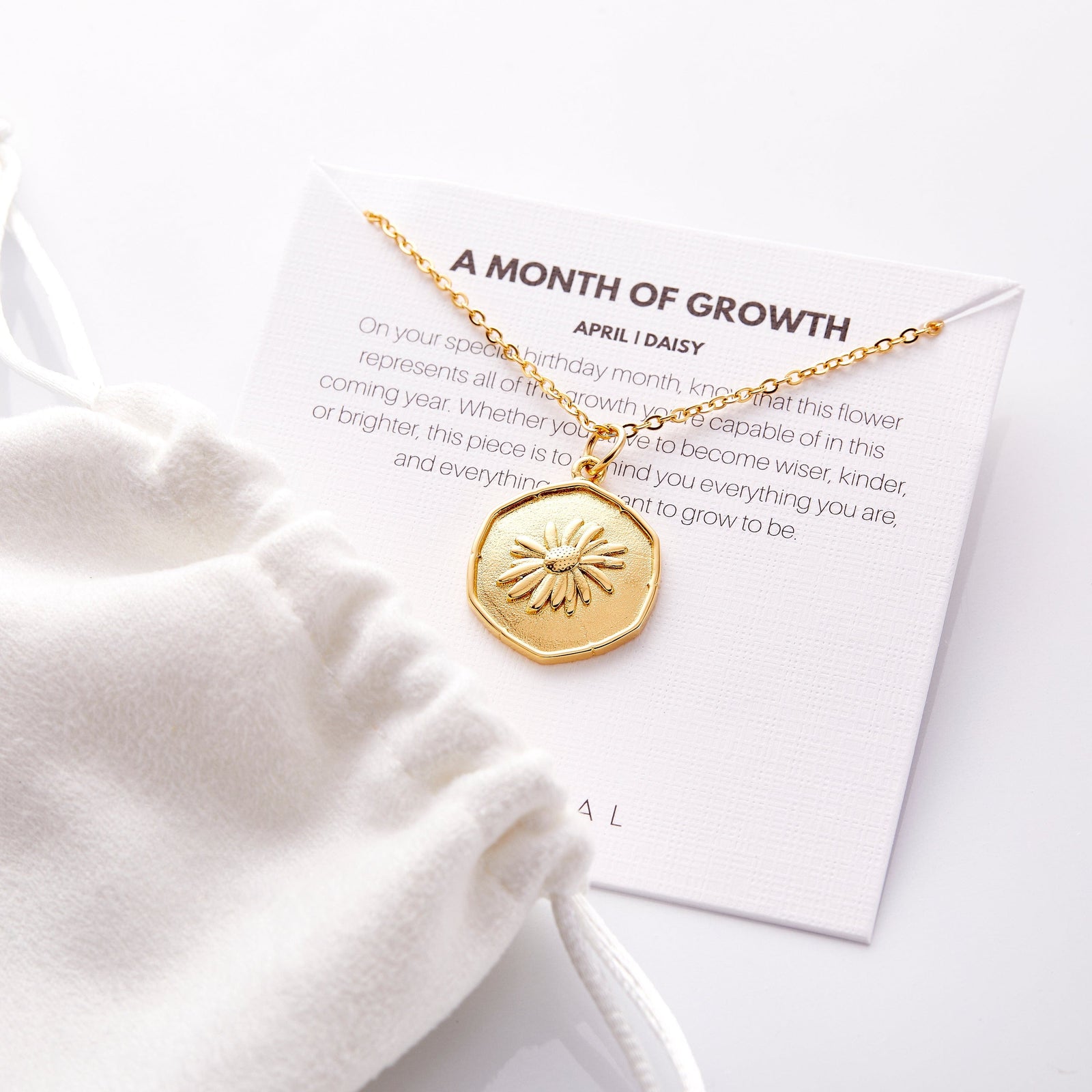 The gold April | Birth Flower Pendant displayed on its packaging that features the description of the jewelry.