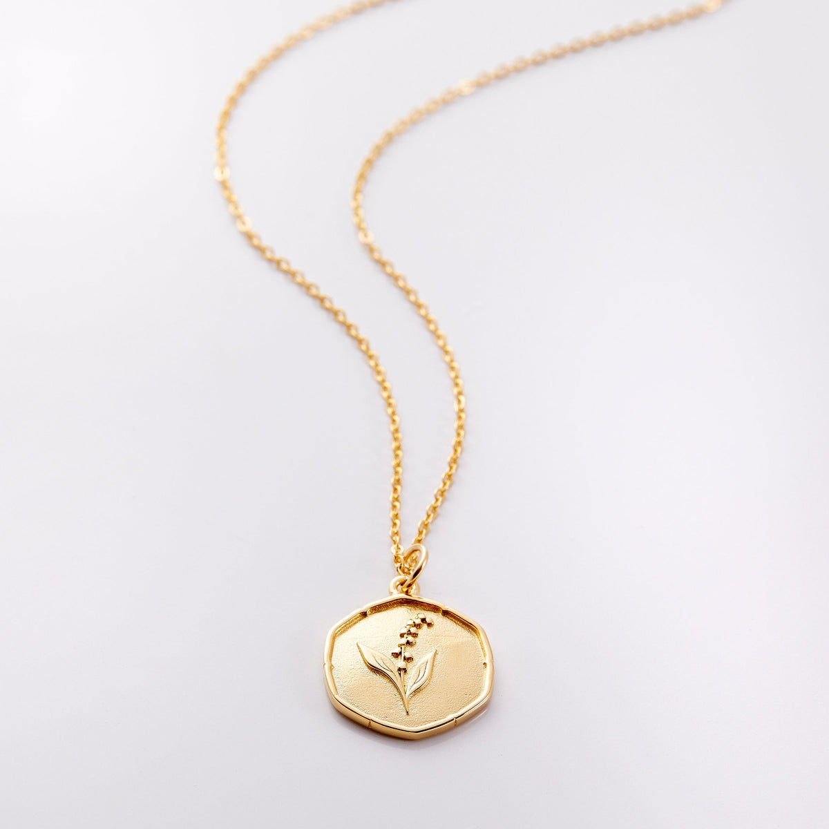 Photo of an 18k golf plated necklace with a pendant that is molded with an imperfect finish, the May Birth Flower is a lily of the valley to represent purity and happiness