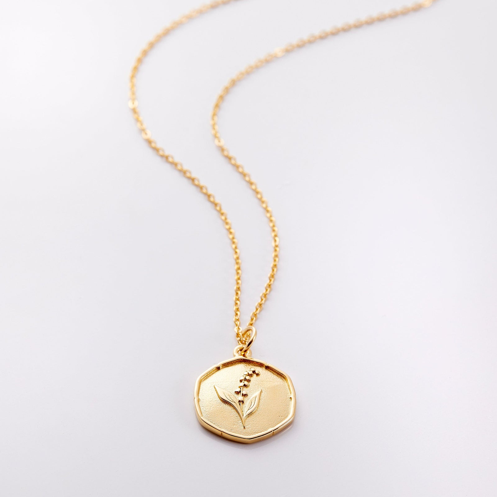 Photo of an 18k golf plated necklace with a pendant that is molded with an imperfect finish, the May Birth Flower is a lily of the valley to represent purity and happiness