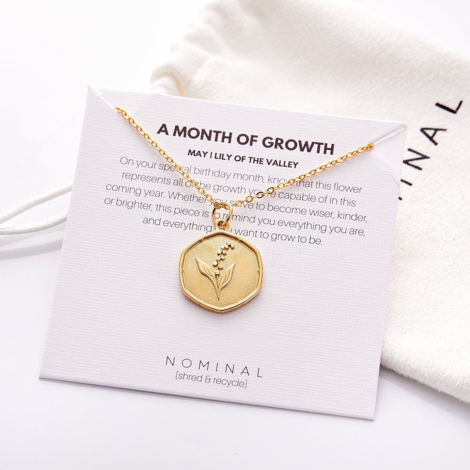 The gold May | Birth Flower Pendant displayed on its packaging that features the description of the jewelry.