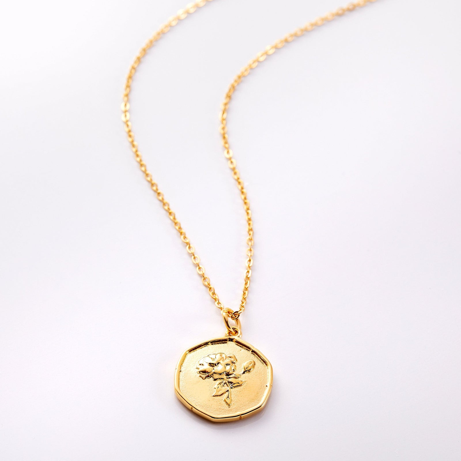 An 18k gold plated necklace laid flat on a light background. The Birth Flower collection highlights the flower of your birth month or the month of a loved one on a vintage-style ridged pendant 