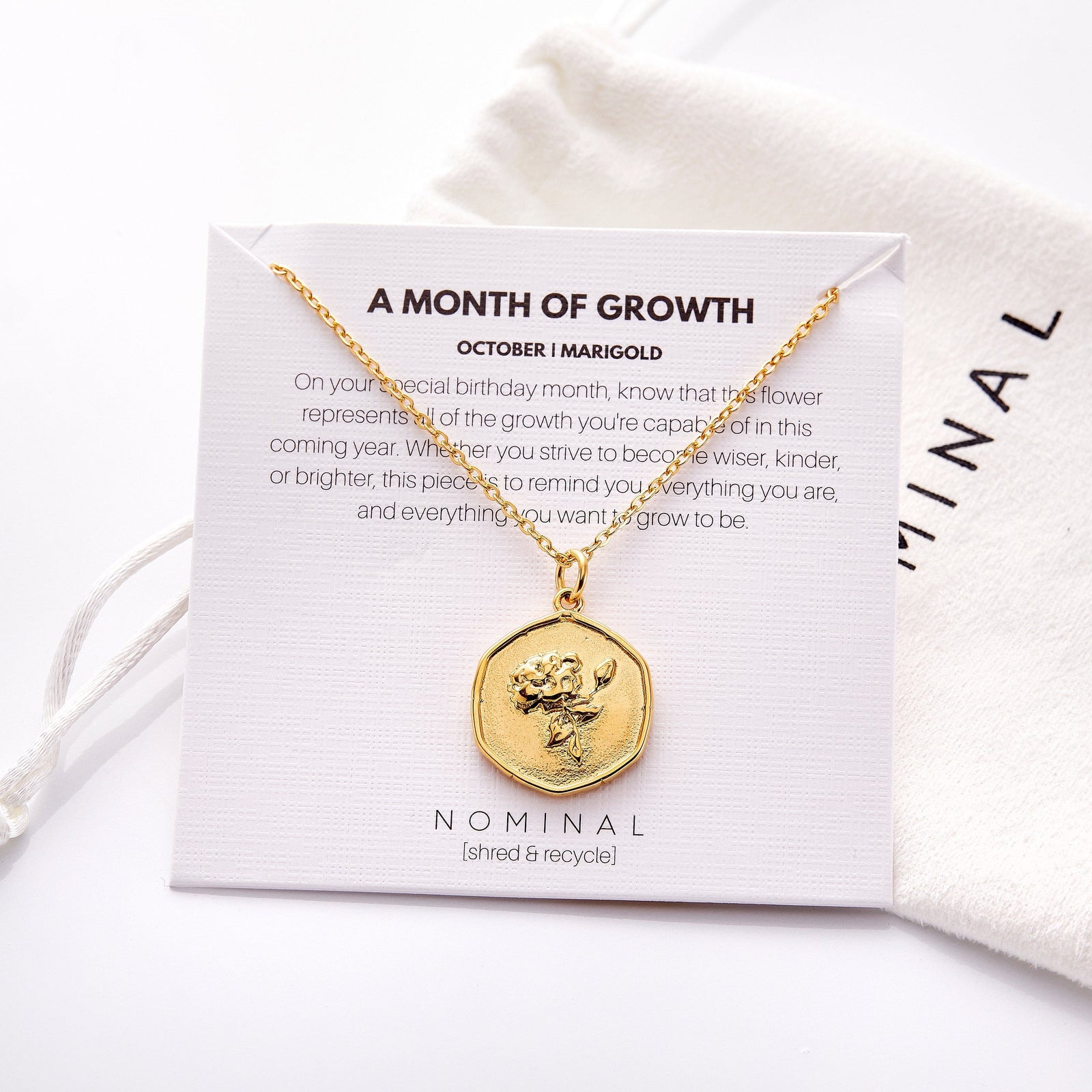 The gold October | Birth Flower Pendant displayed on the Nominal packaging that also features the description of the jewelry.