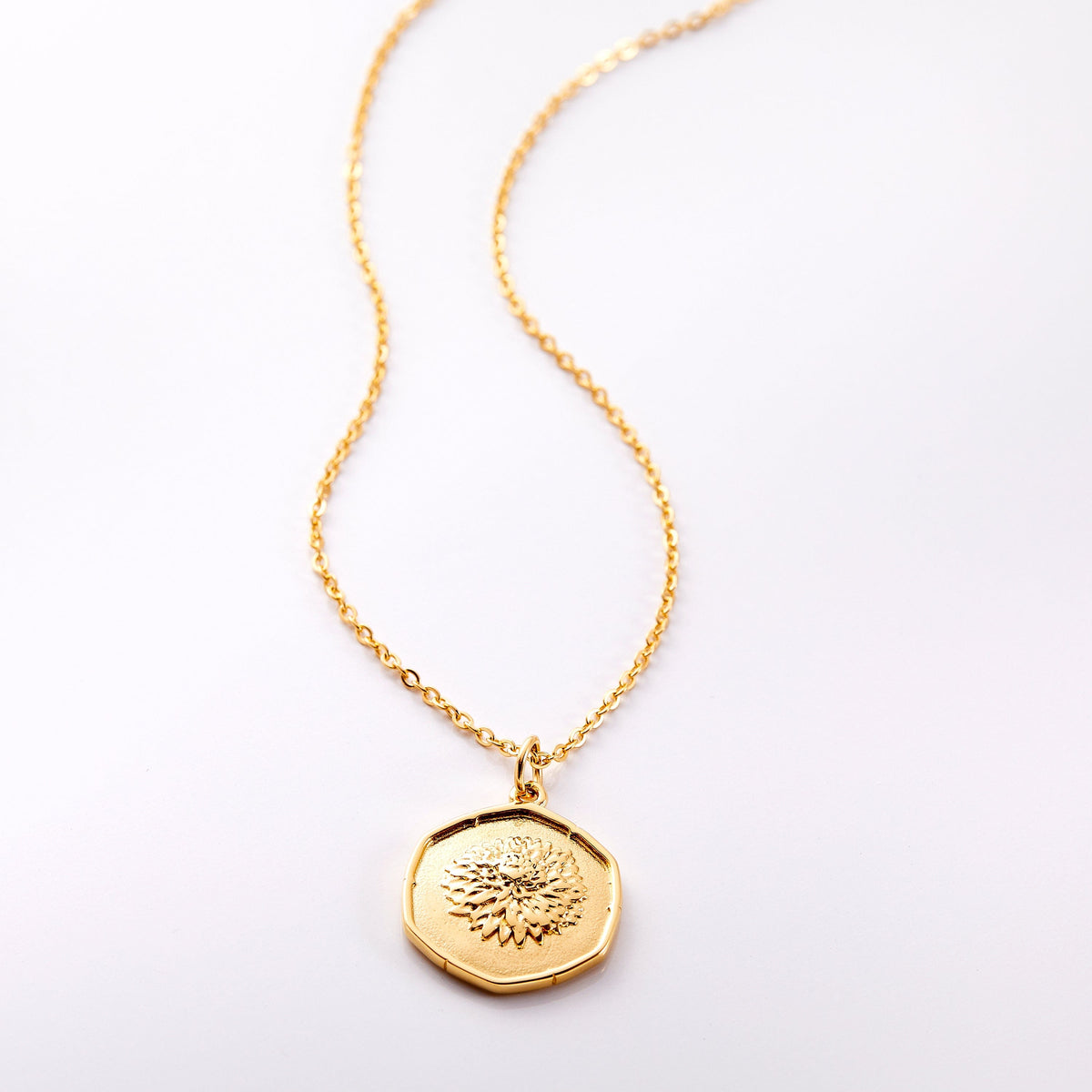 An 18k gold plated necklace laid flat on a light background. The Birth Flower collection highlights the flower of your birth month or the month of a loved one on a vintage-style ridged pendant 