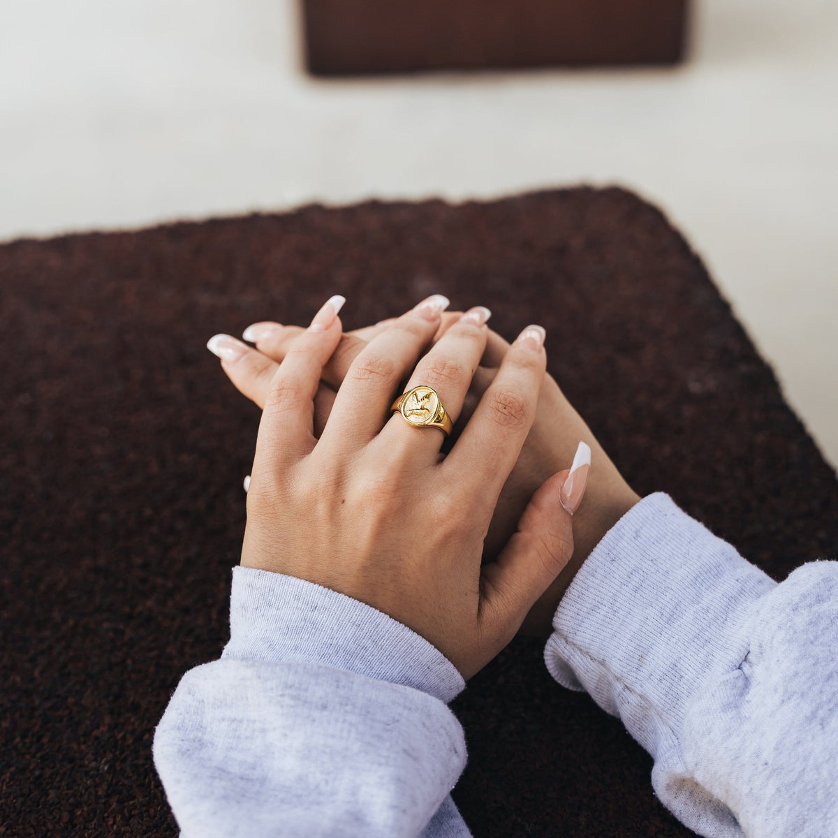 Woman wearing a gold ring of tranquility with a raised dove engraving, styled with a light gray long-sleeve top. 
