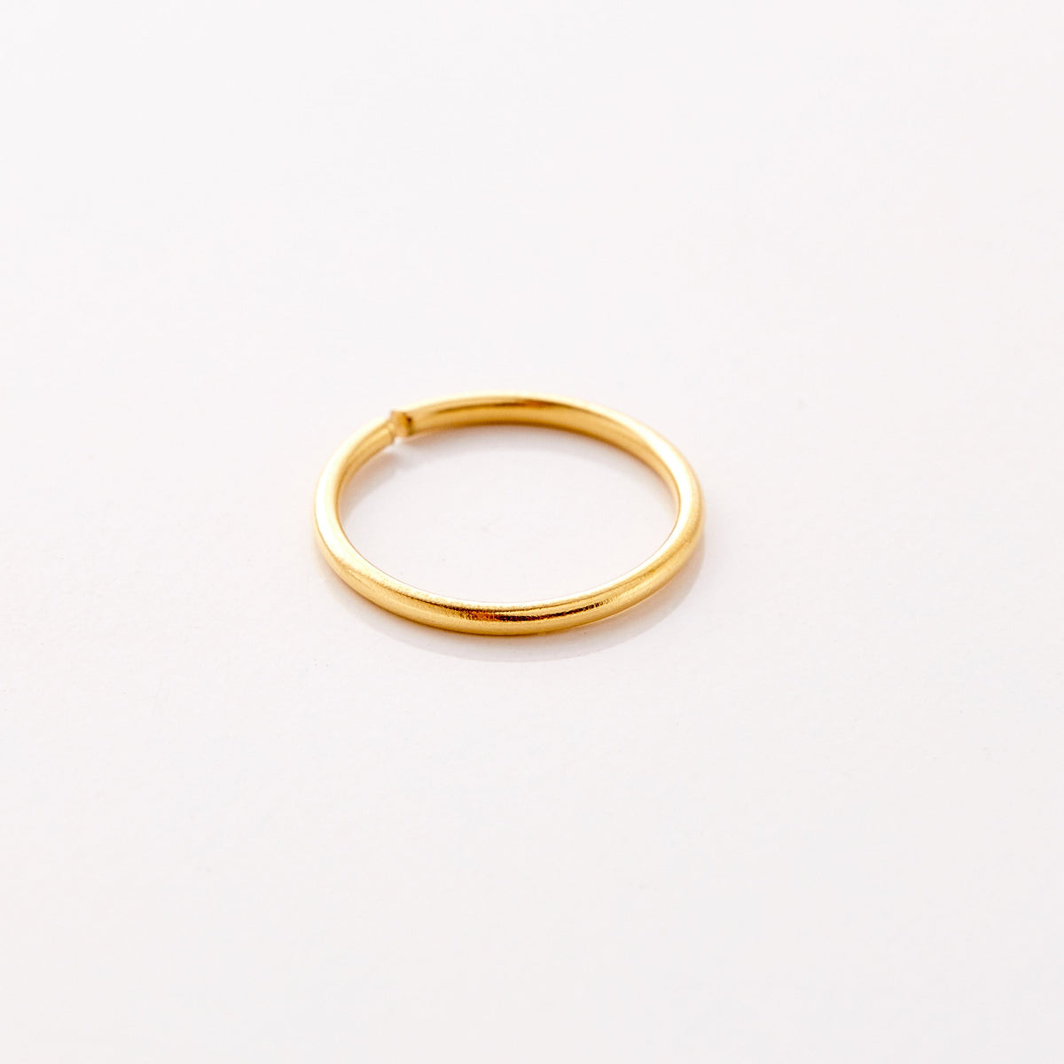 Photo of an 18k gold plated minimalistic nose hoop against a light background.