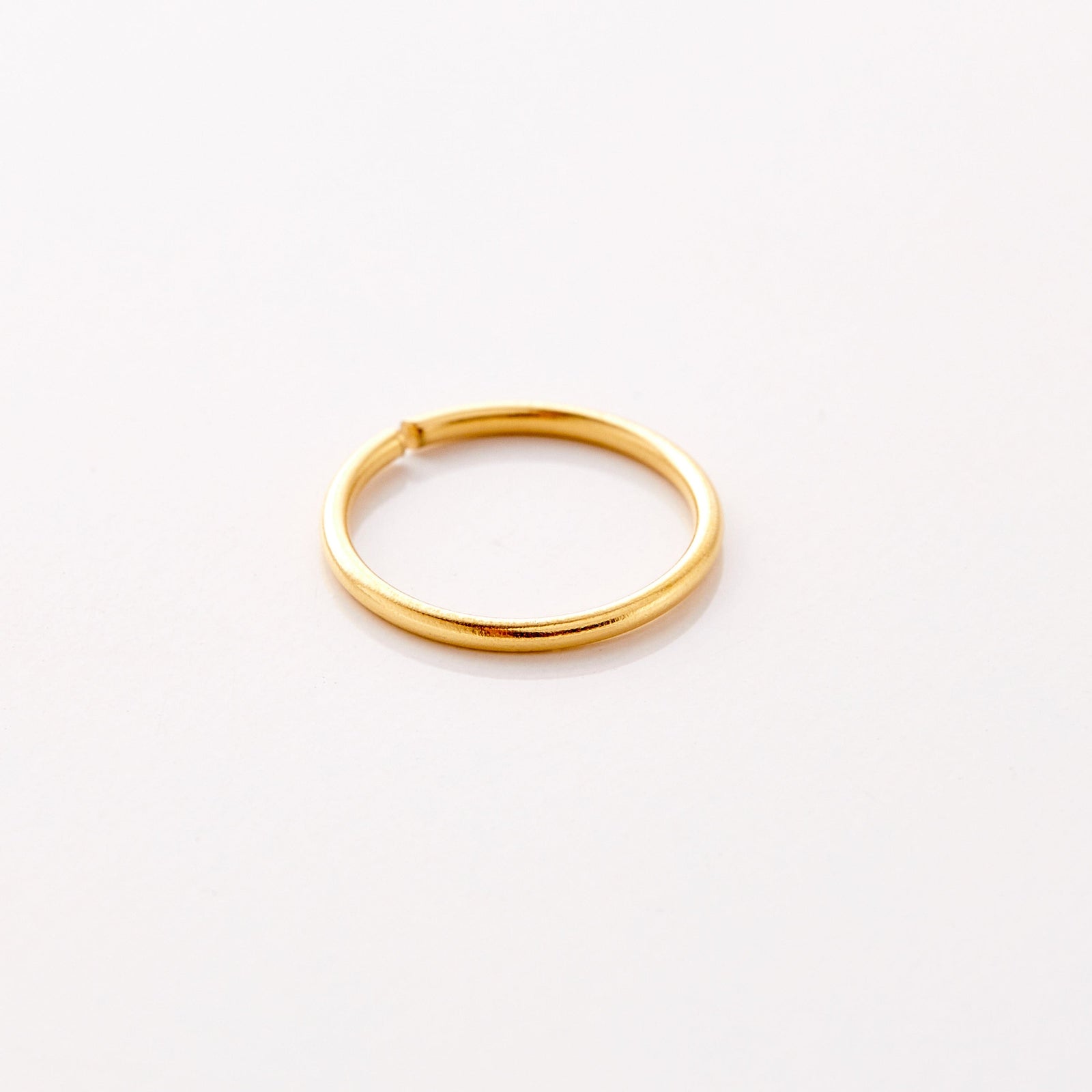 Photo of an 18k gold plated minimalistic nose hoop against a light background.