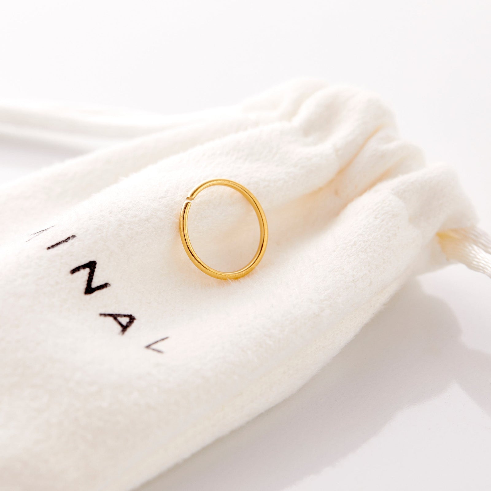 The gold Classic Nose Hoop laid flat against the Nominal pouch.