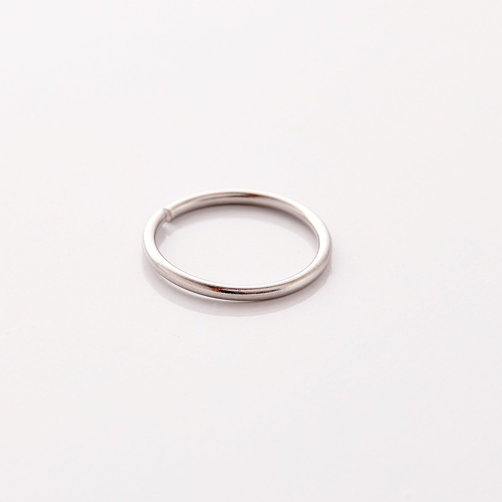 Photo of a silver minimalistic nose hoop against a light background.