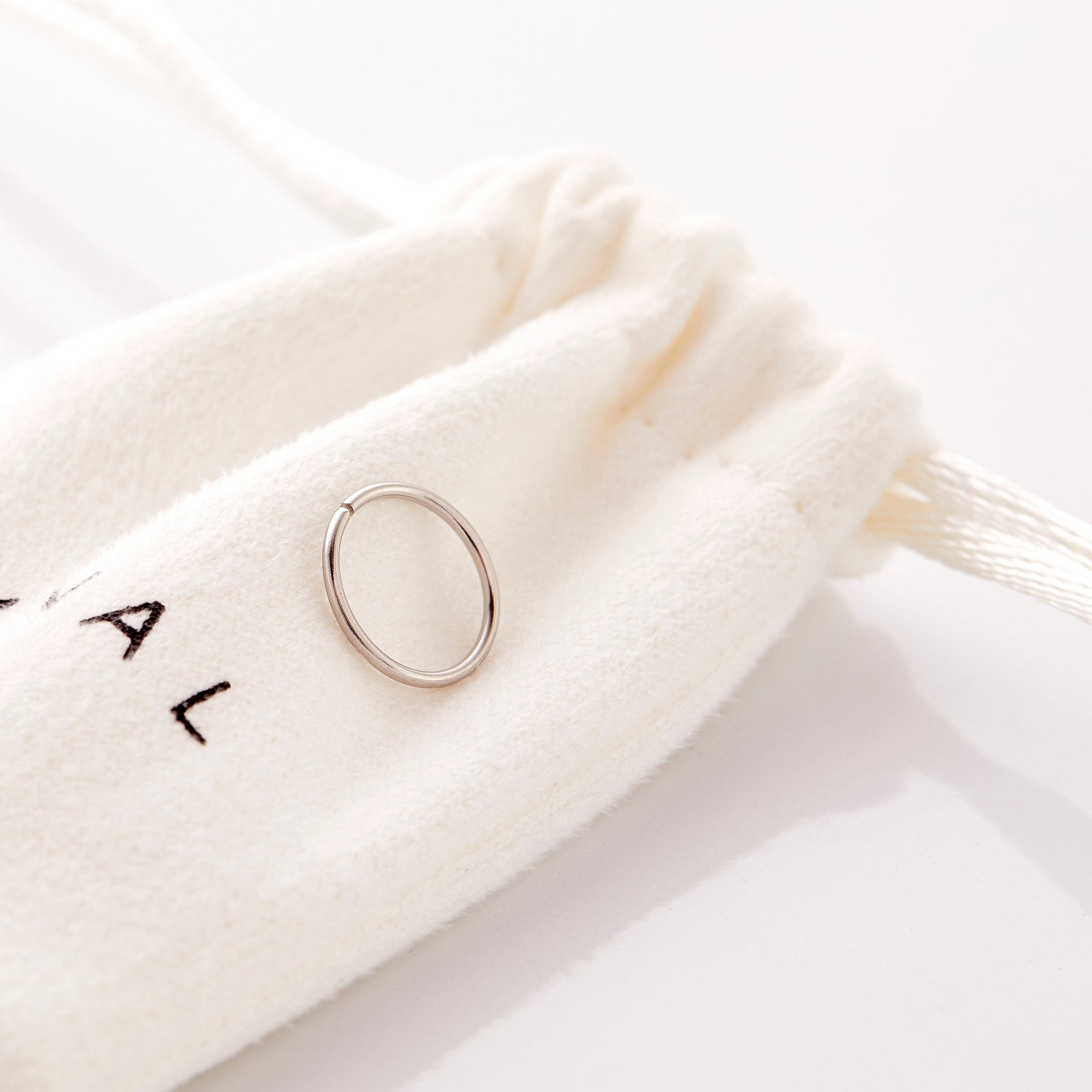 The silver Classic Nose Hoop laid flat against the Nominal pouch.