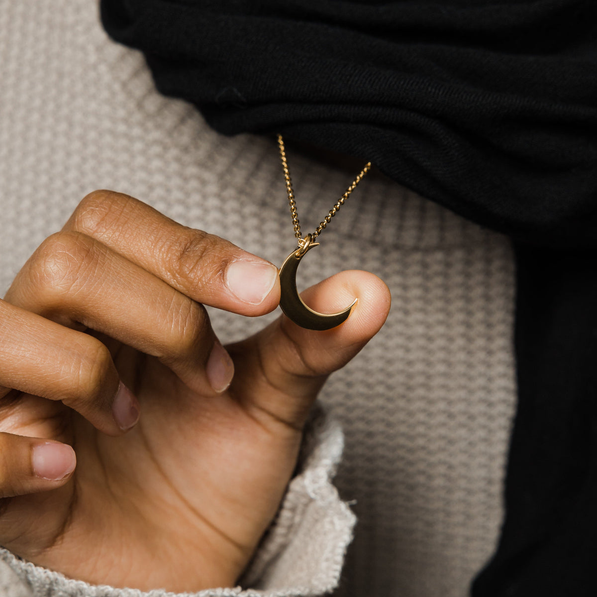 Close up of the gold Crescent Necklace as the model holds the pendant.