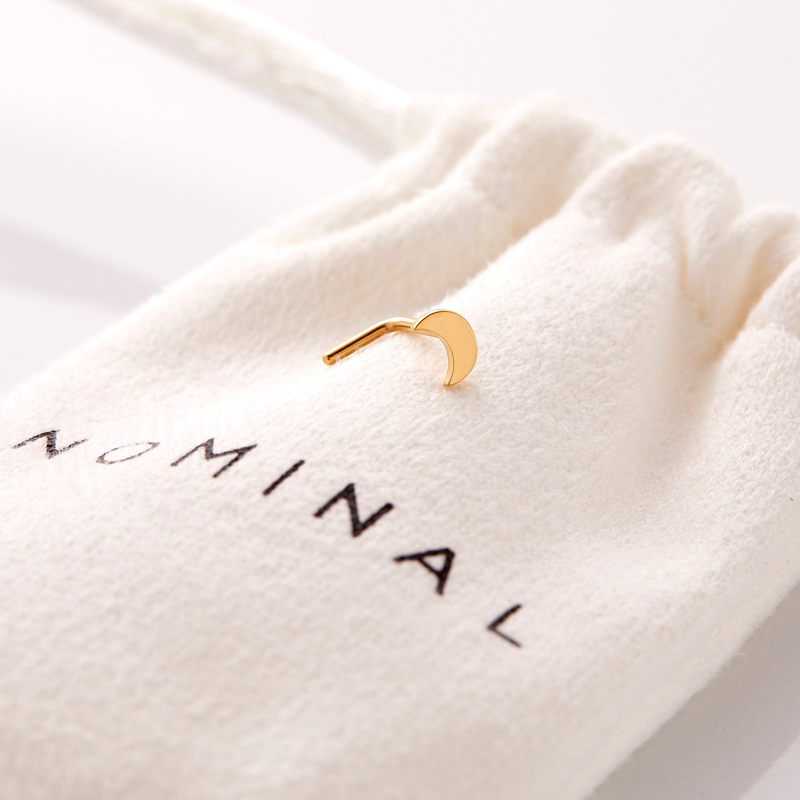 the gold Crescent Stud Nose Ring resting on the Nominal pouch