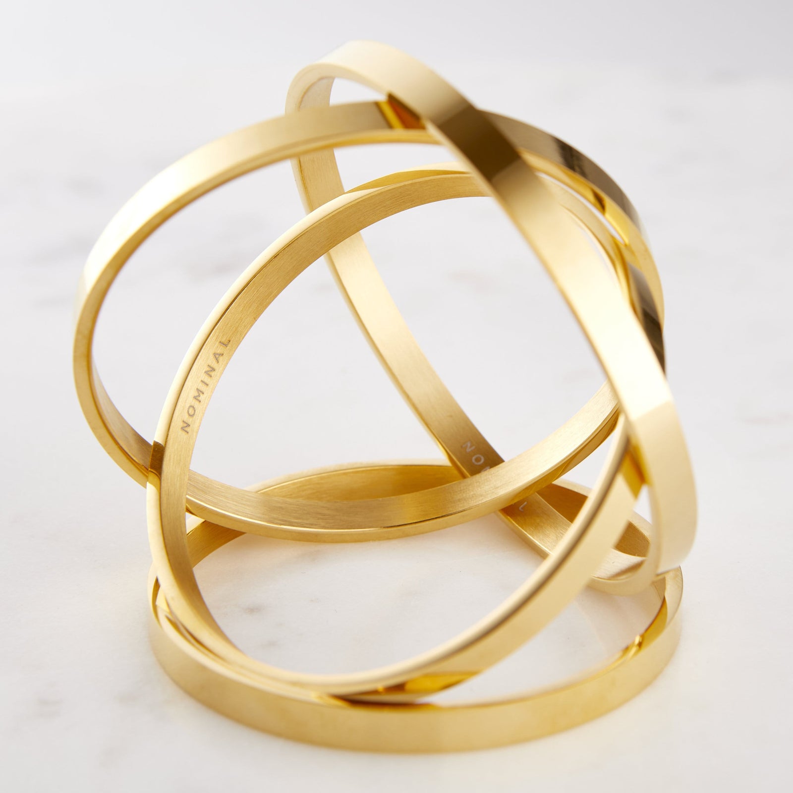 Photo of four pieces of the gold essential bangle resting against each other showing the jewelry's different angles.