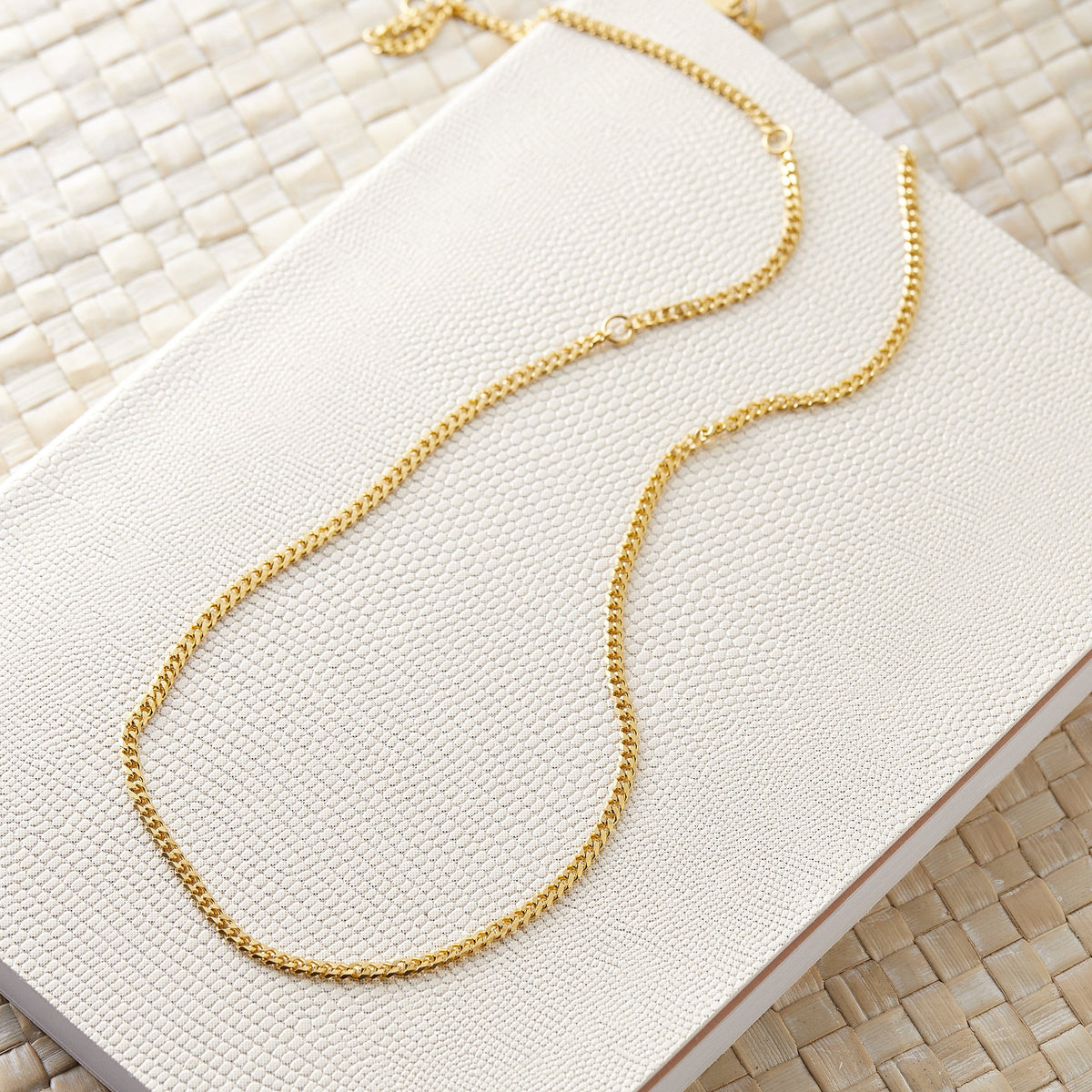 A gold Cuban chain laid flat on a cream woven surface.
