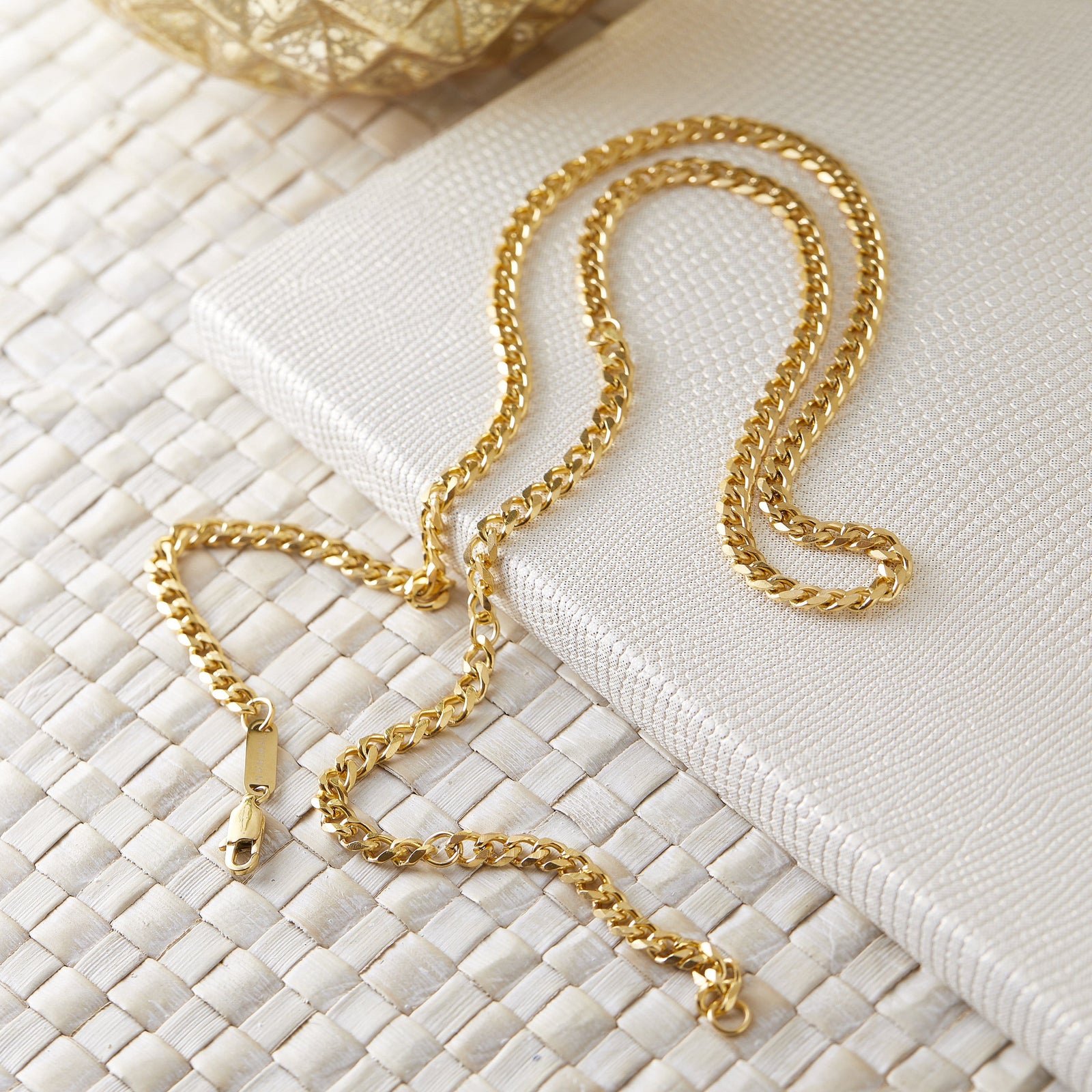Gold Cuban chain laid flat on a cream textured surface.