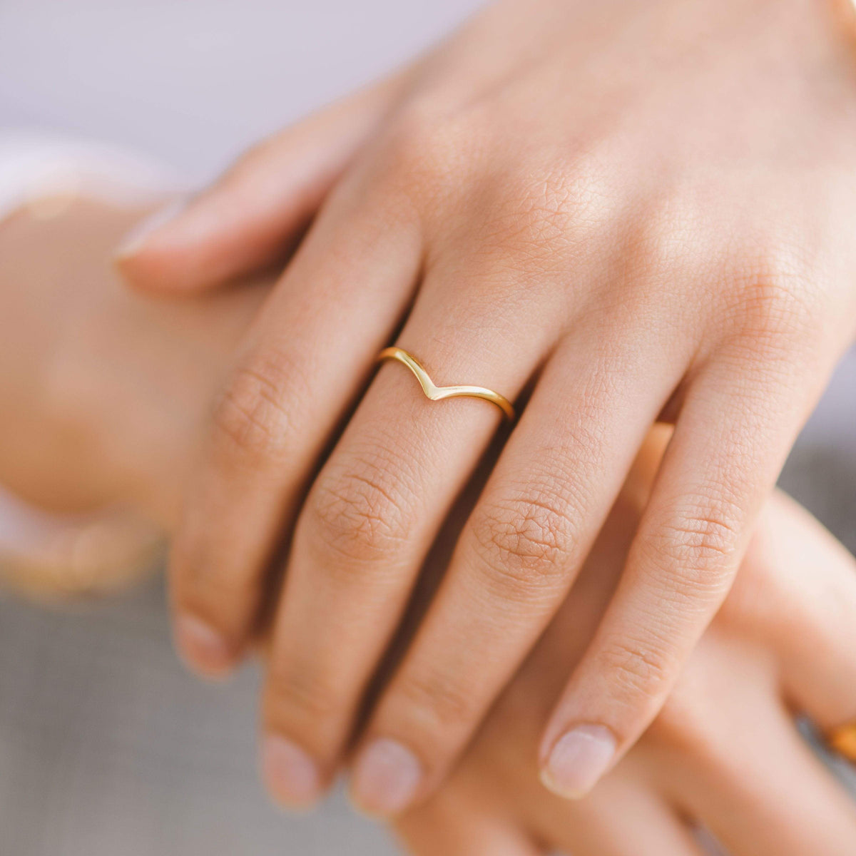 Gold completion ring worn on the middle finger, hands overlapping in a relaxed pose.