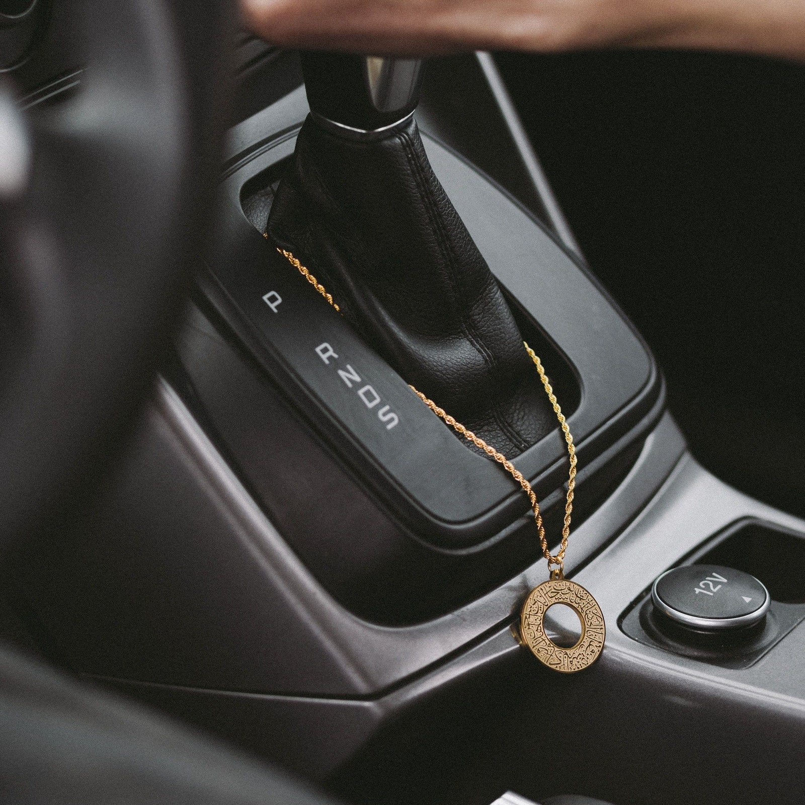 Gold Duaa Al-Safar car hanger draped on the gear shift in a car interior.