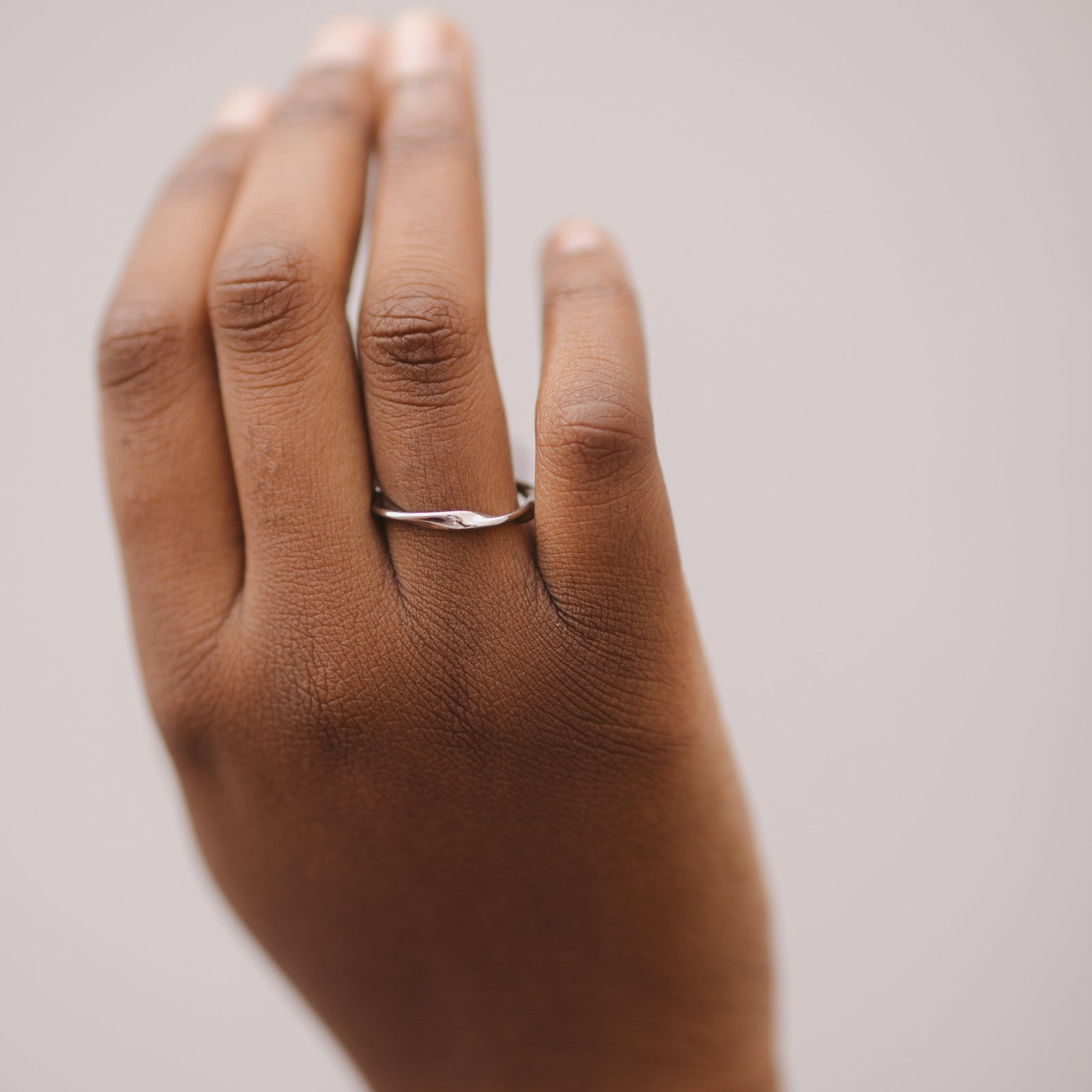 Silver ripple ring worn on the ring finger, displayed against a soft, neutral background.
