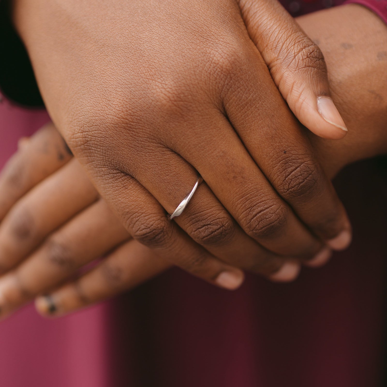 Close-up of hands together, one wearing a silver ripple ring against a maroon outfit.